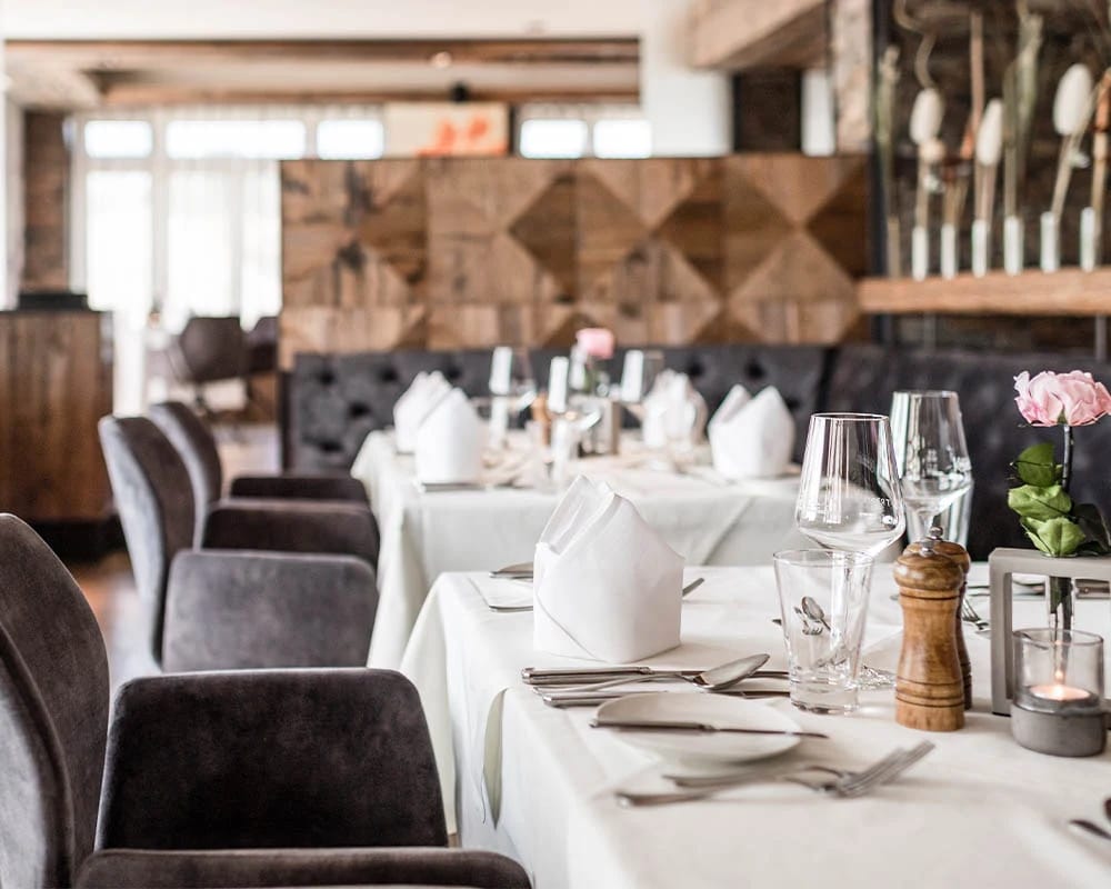 Restaurant mit eingedeckten Tischen, Polsterstühlen und Holzwand