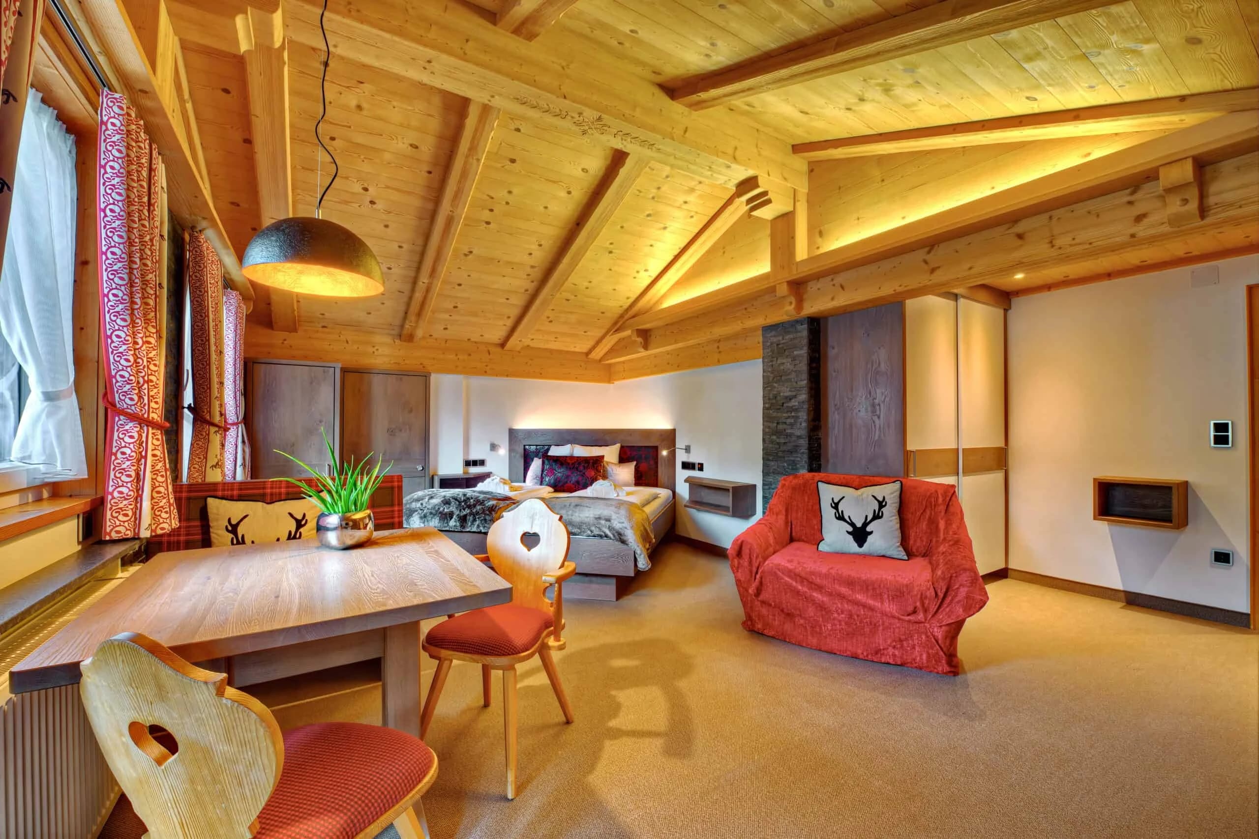 Studio mit Holzdecke, rotem Sessel, Esstisch und Doppelbett