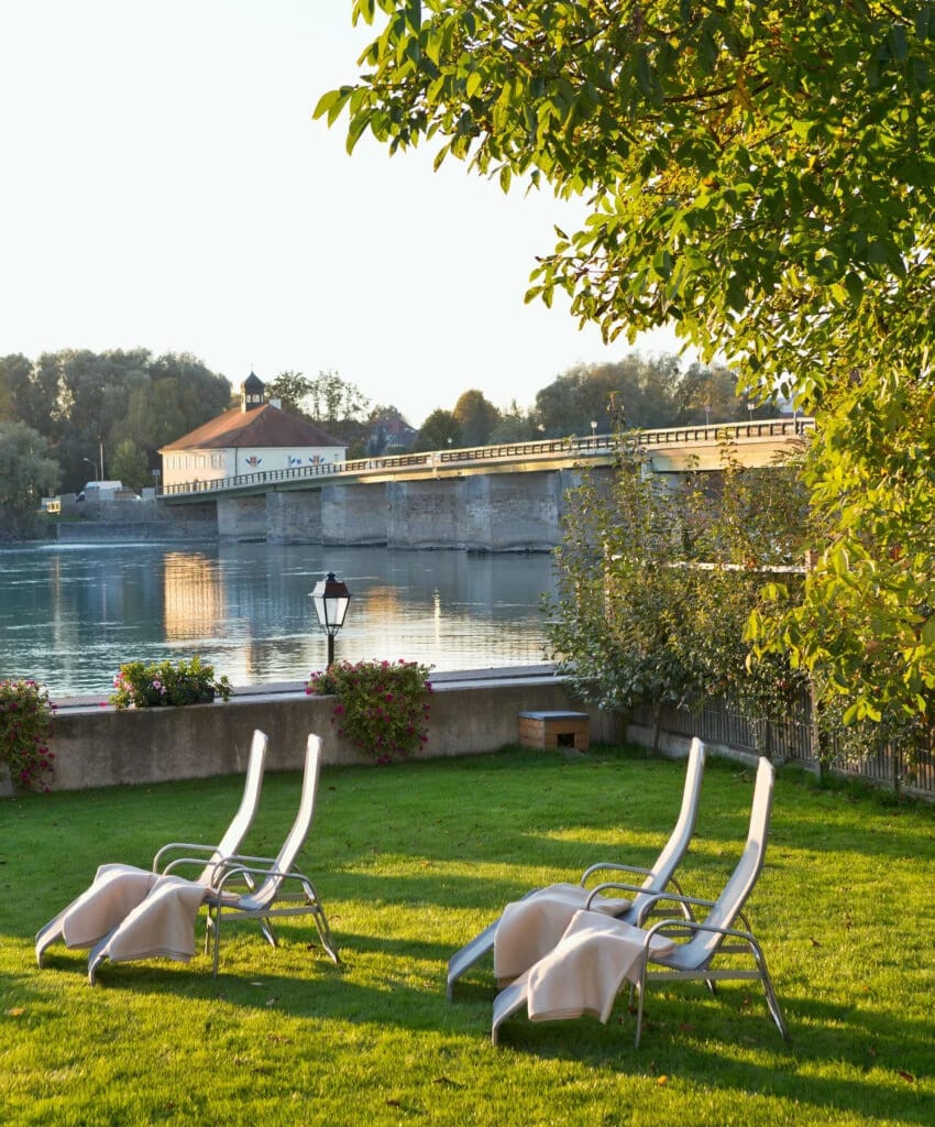 Liegewiese mit Sonnenliegen am Flussufer, im Hintergrund eine Brücke