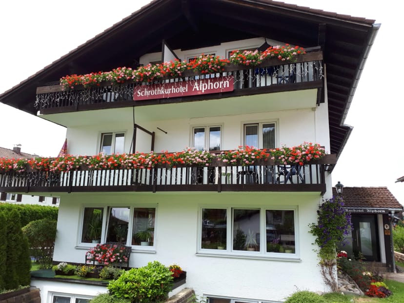 Weißes Hotelgebäude mit dunklen Holzbalkonen voller roter Geranien und dem Schriftzug Schrothkurhotel Alphorn
