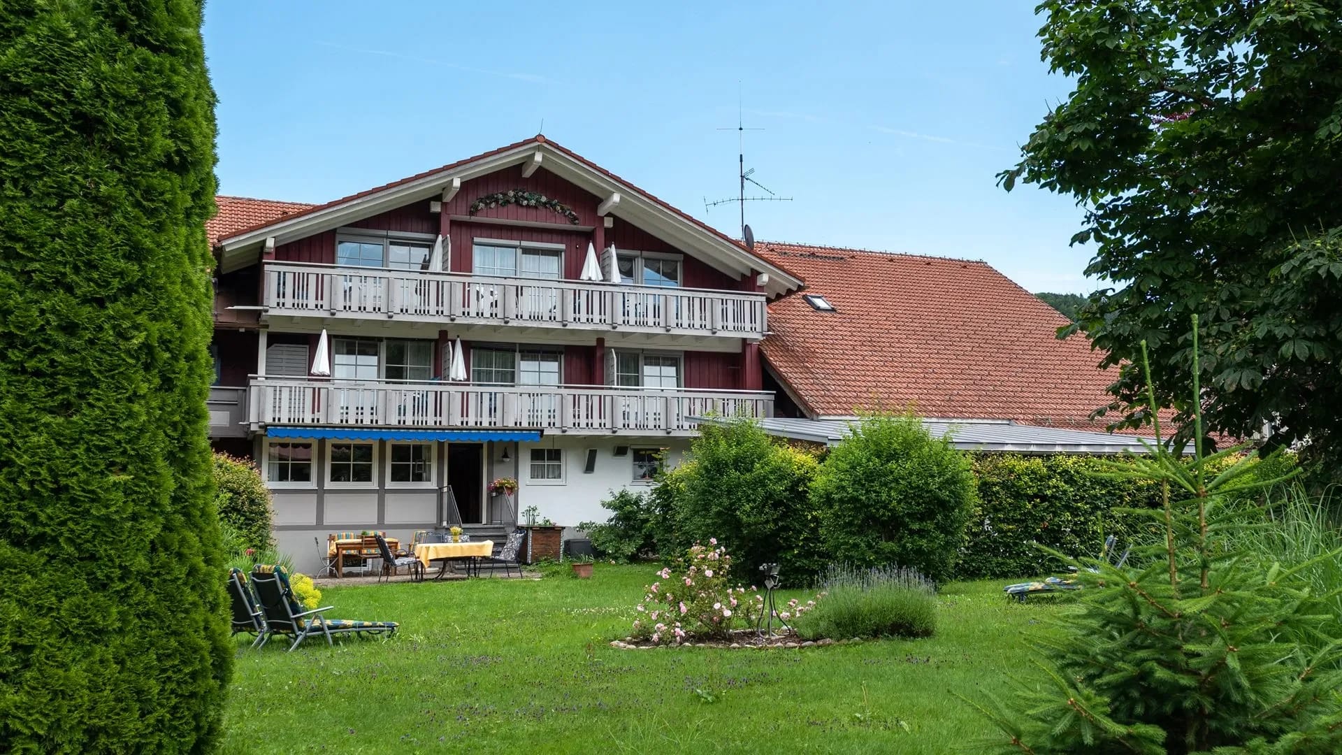 Gartenseite des Hauses mit Holzbalkonen, davor Rasenfläche mit Liegestühlen und einer Sitzgruppe
