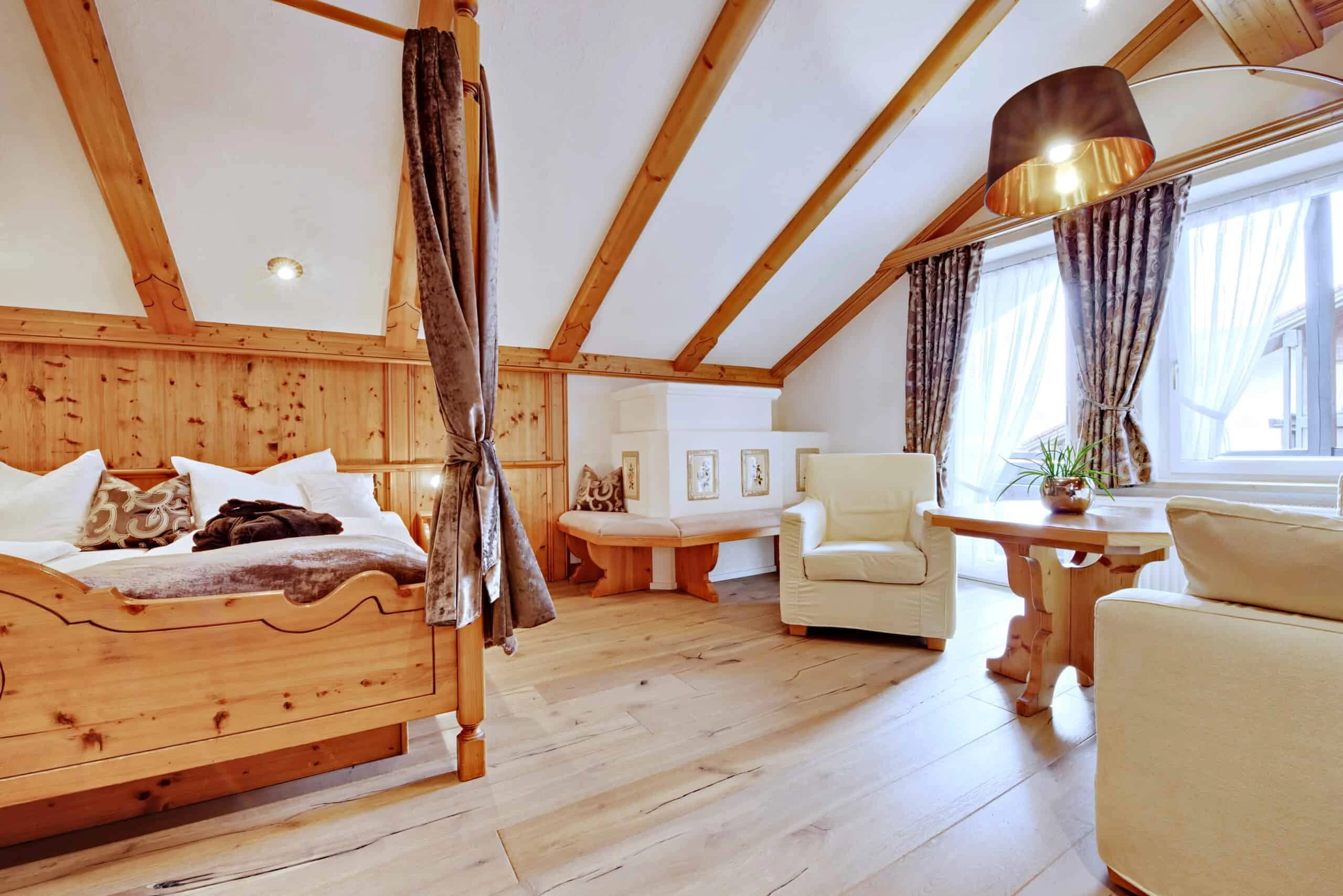 Dachzimmer mit Holzbett unter offenem Dachstuhl, Sesseln und Sitzecke am Fenster