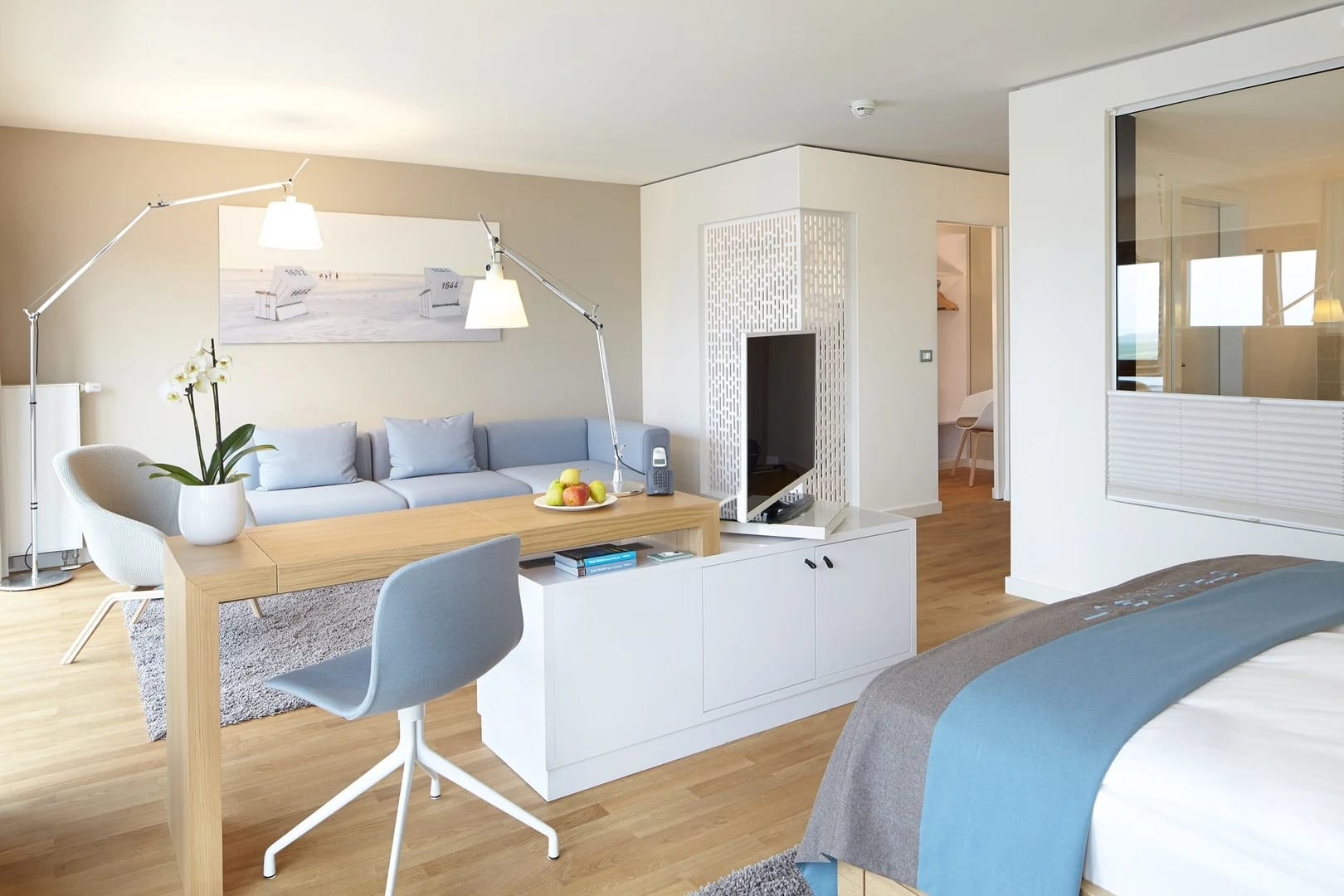 Suite mit Schreibtisch, Sofa und Bett, getrennt durch eine halbhohe Raumteilerwand