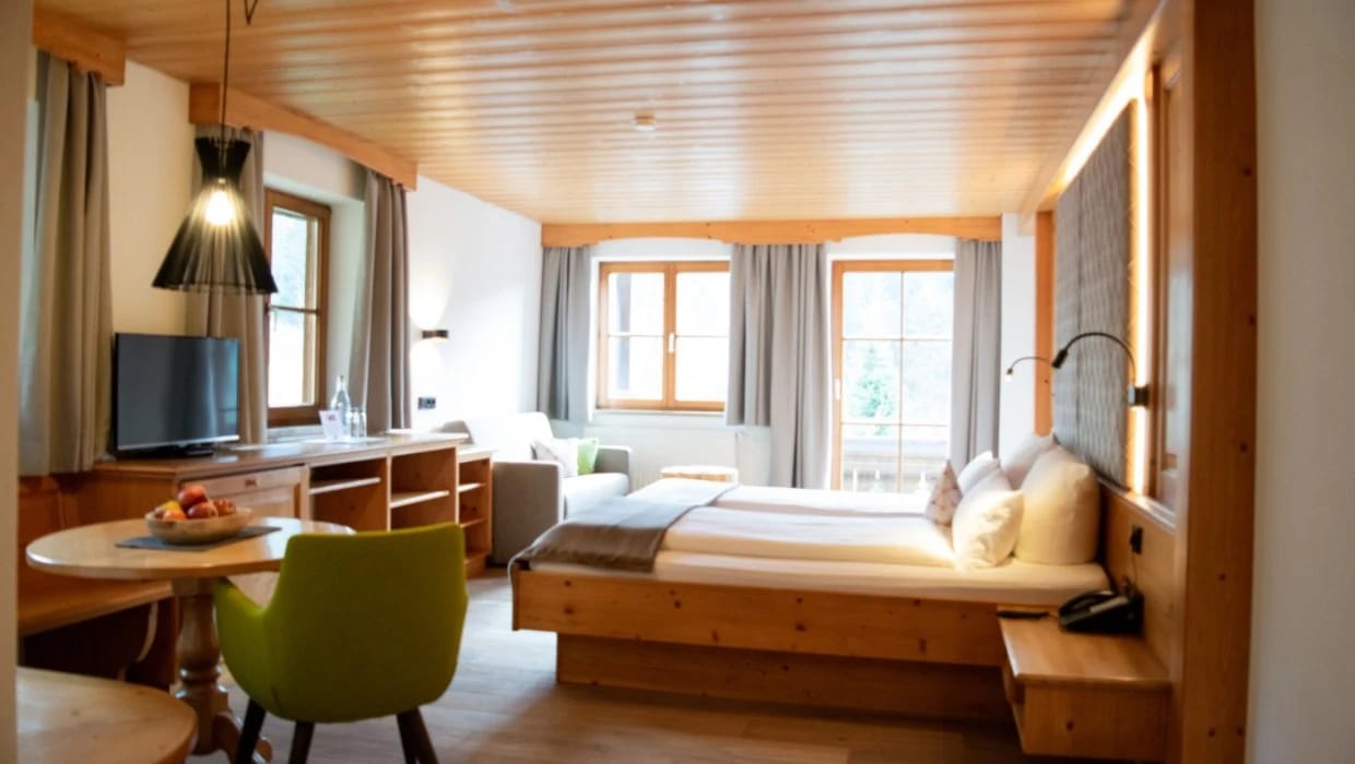 Zimmer mit Sitzbereich, Schreibtisch und großen Fenstern