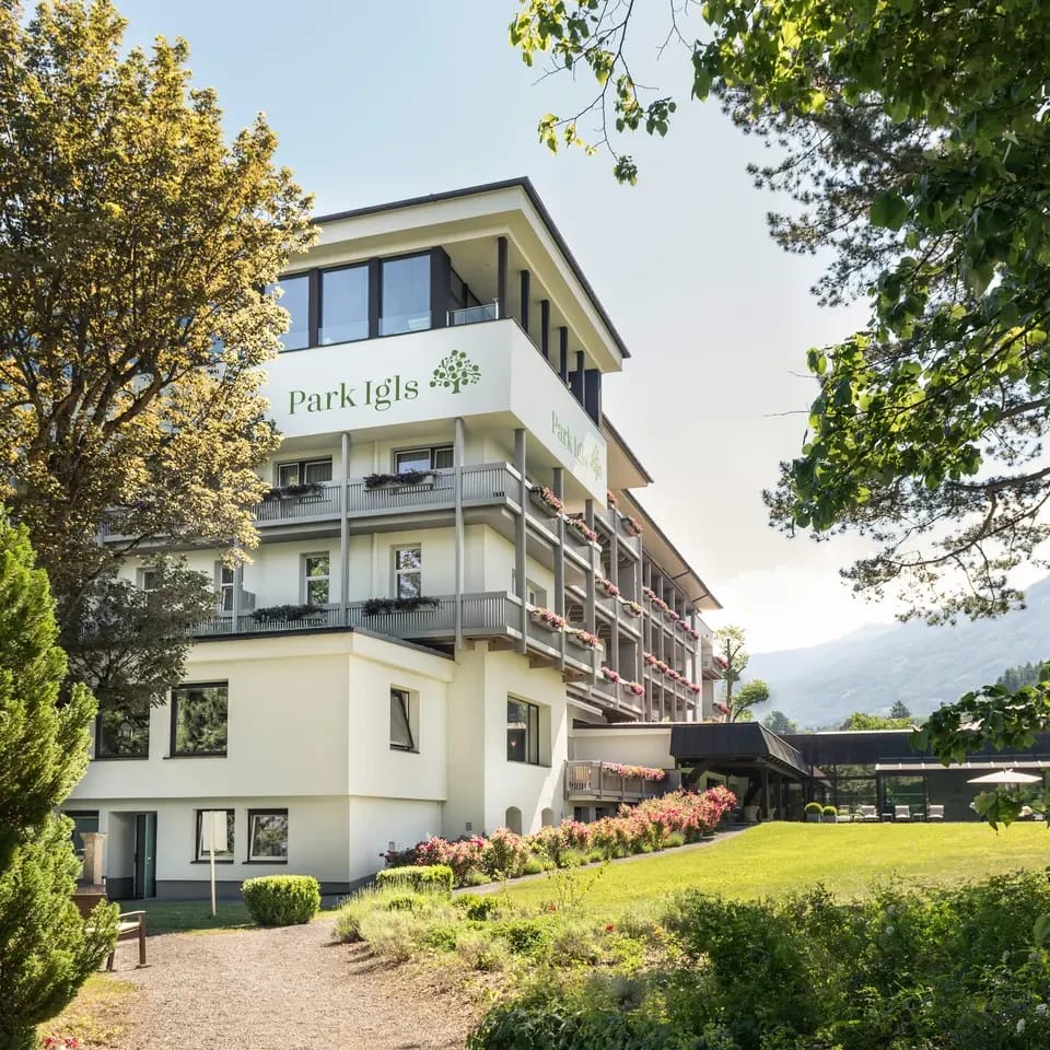 Hotelgebäude mit Schriftzug Park Igls, Balkonen und Gartenweg zwischen Bäumen
