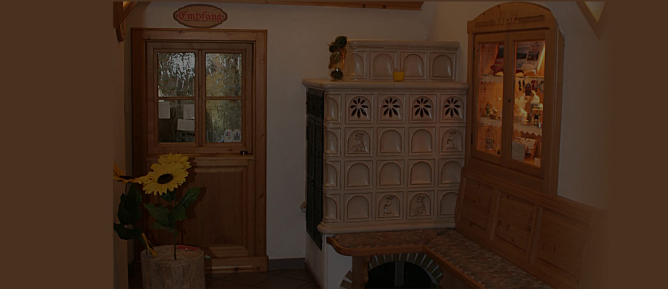 Gemütliche Stube mit Kachelofen, Holztür und Sonnenblumen