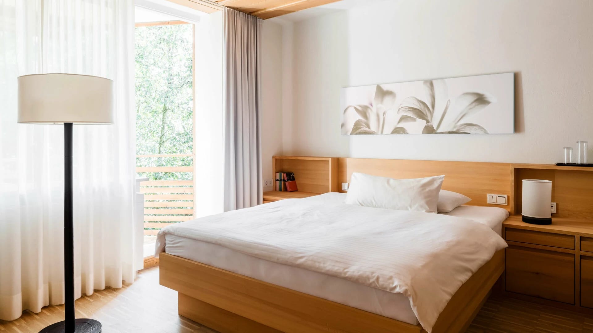 Zimmer mit Doppelbett, Holzmöbeln, Stehlampe und Fenster mit Vorhang