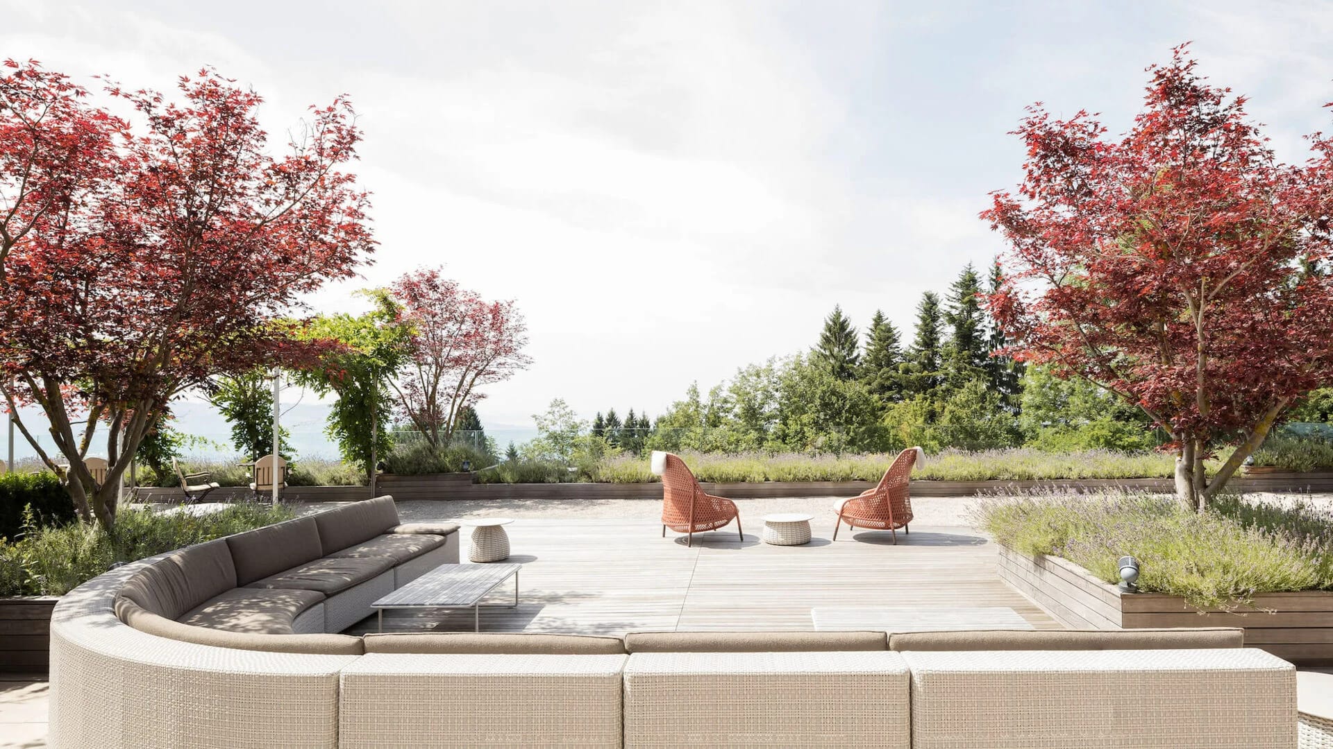 Gartenterrasse mit runder Loungebank, Sesseln und rotlaubigen Bäumen