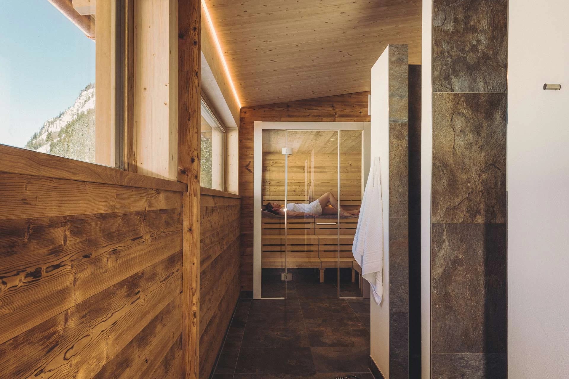 Wellnessgang aus Holz und Naturstein mit Fensterfront und Blick in die Saunakabine