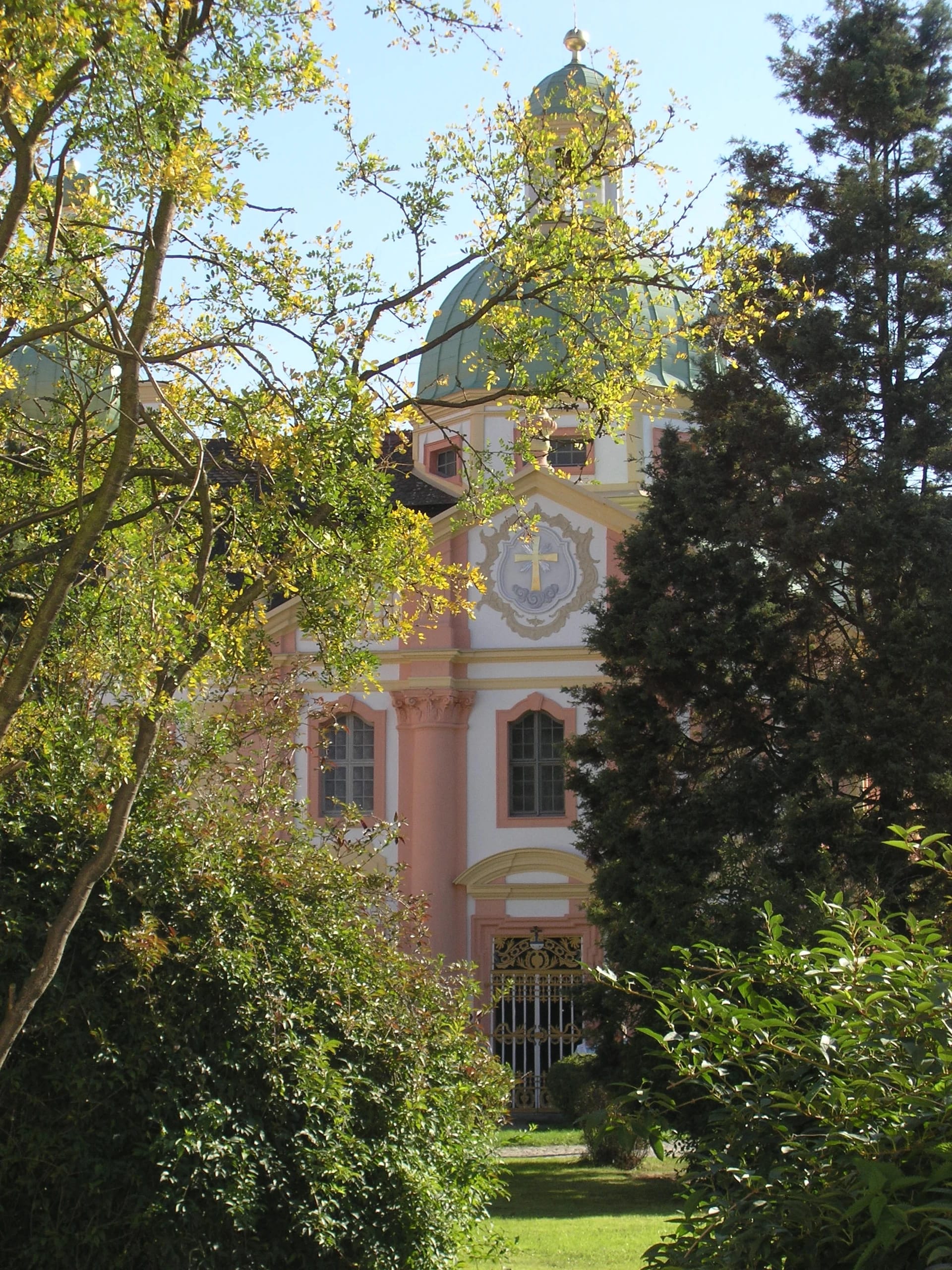 Grün gedeckte Kirchenkuppel und rosafarbene Fassade zwischen herbstlich gefärbten Bäumen