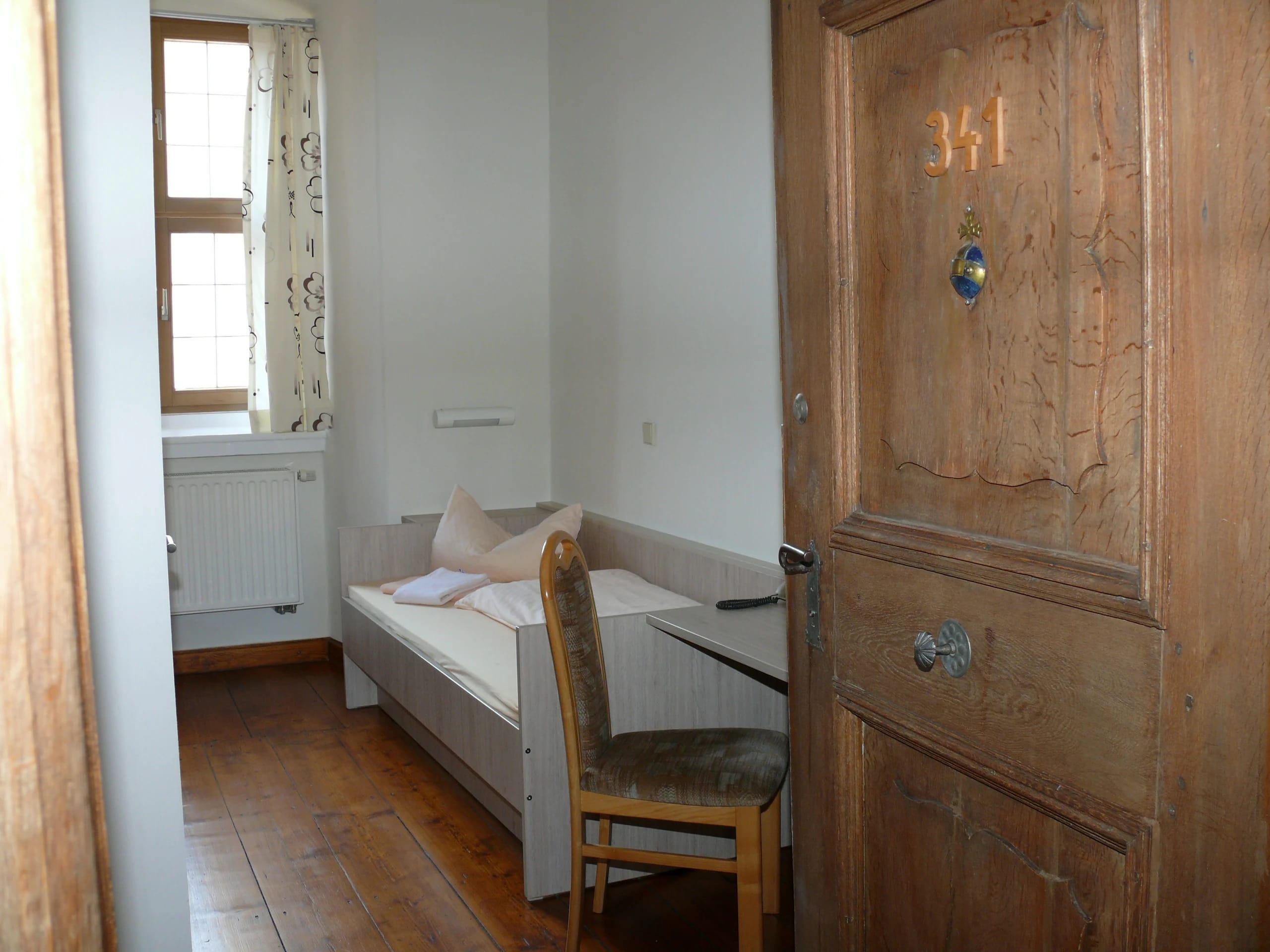 Gästezimmer mit Einzelbett, Holzdielen und historischer Zimmertür mit Nummernschild