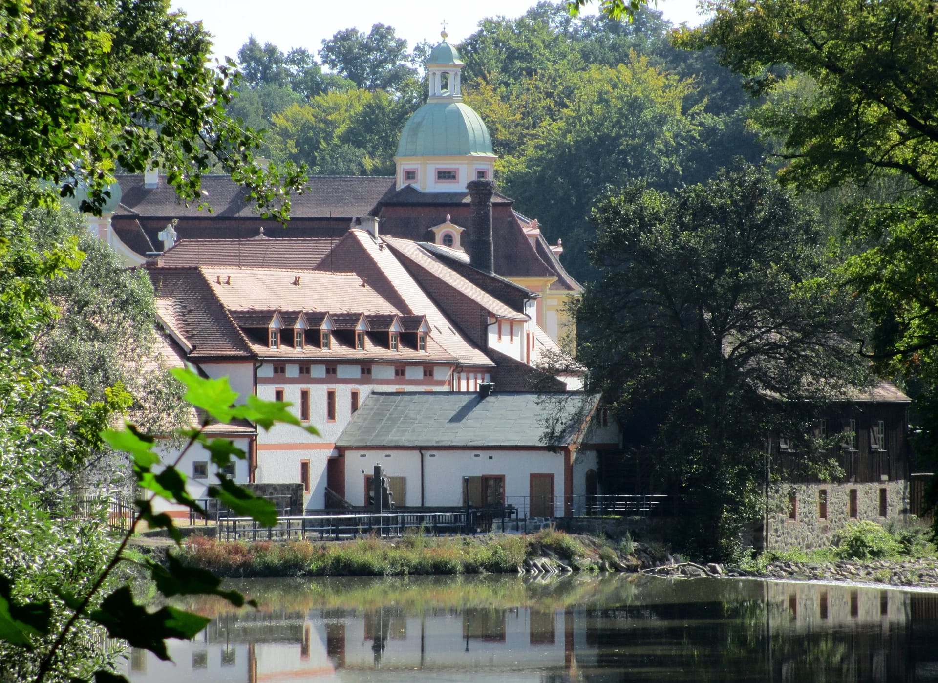 Blick über die Neiße auf die Klostergebäude zwischen sommergrünen Bäumen