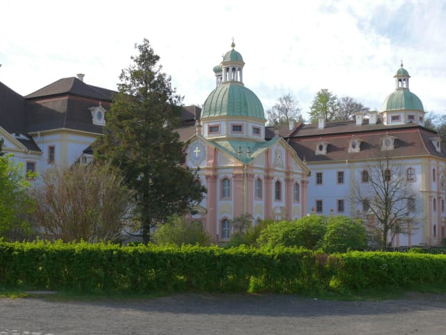 Barocke Klosteranlage mit grün gedeckten Kuppeln hinter Rasenfläche und Hecke