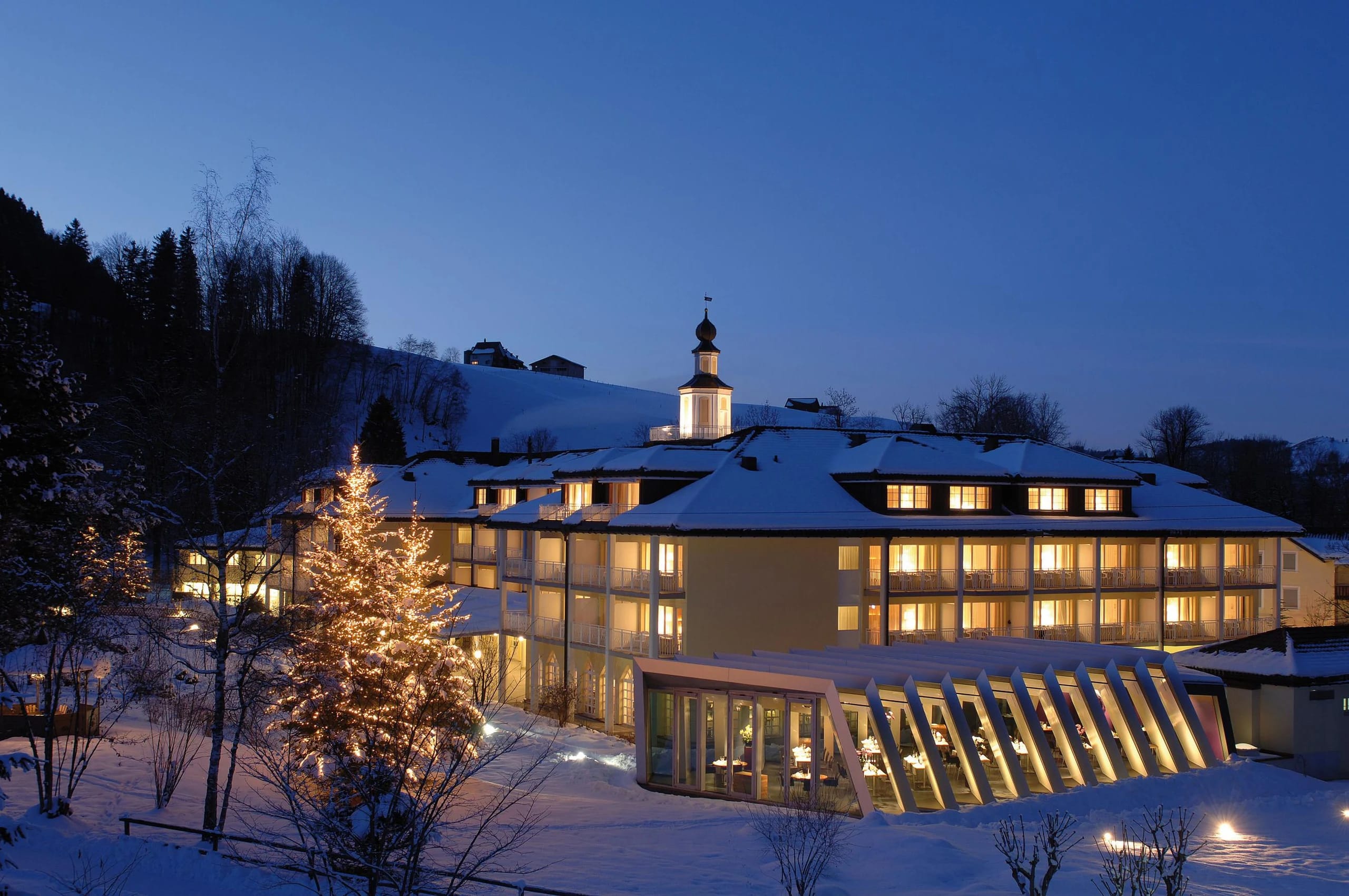 Winterliches Abendpanorama des Haupthauses mit Schnee, Kirchturm und Weihnachtsbeleuchtung