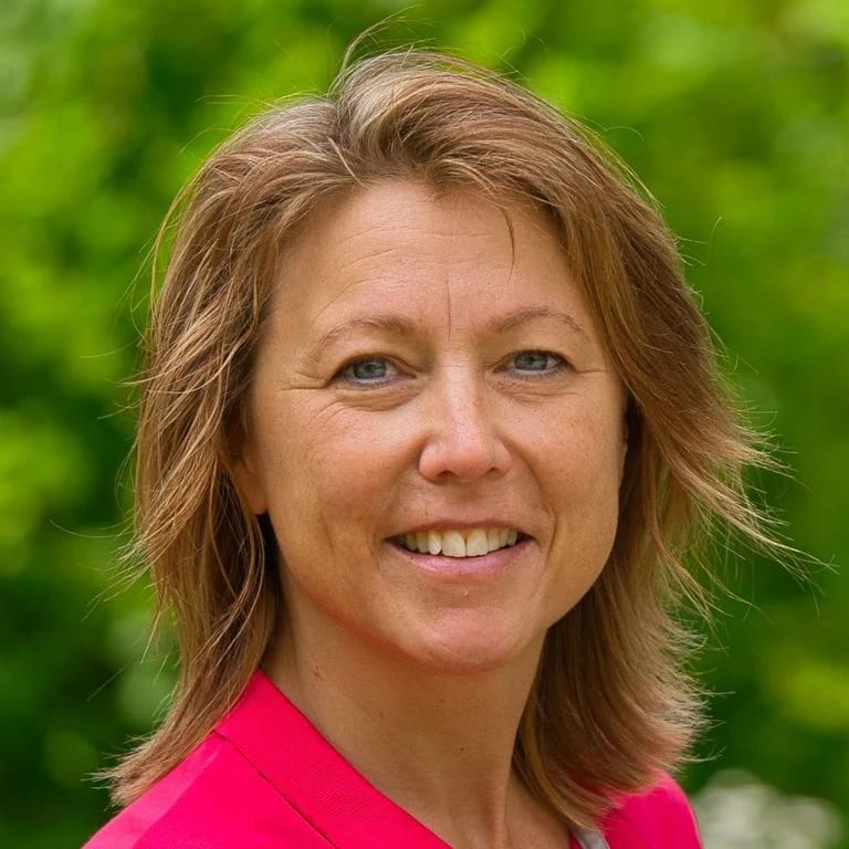 Porträt von Christiane Hefner, lächelnd vor grünem Blätterhintergrund