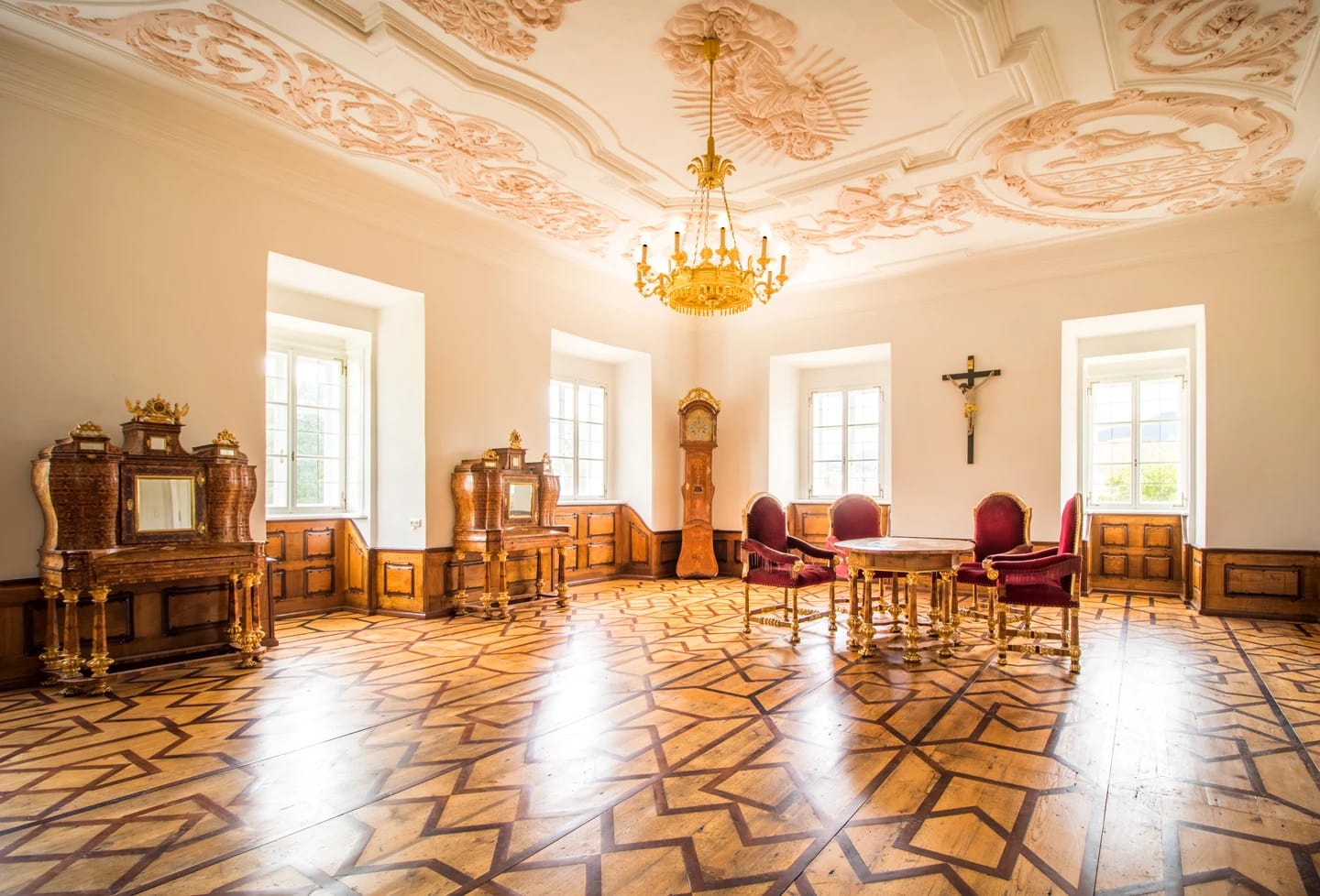 Barocker Salon mit Stuckdecke, Luster, Parkettboden und roten Polstersesseln