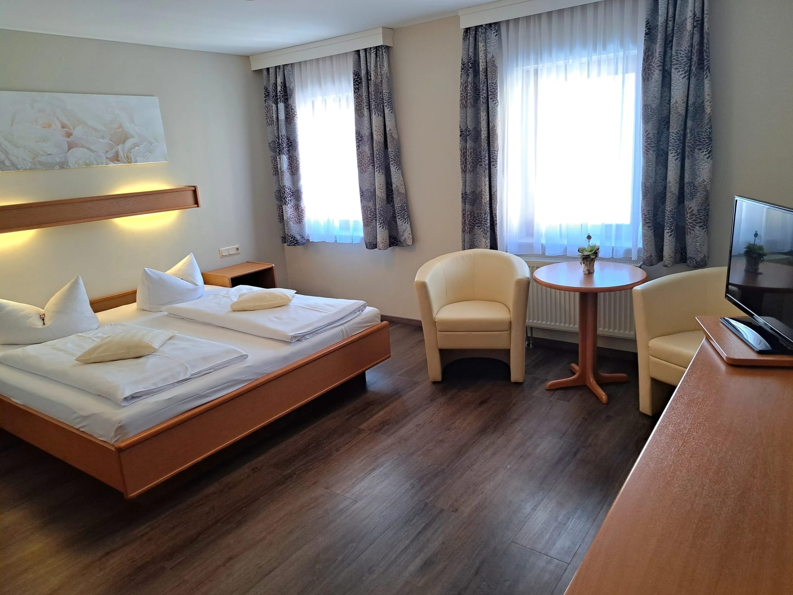 Helles Hotelzimmer mit Doppelbett, zwei Sesseln, rundem Tisch und Fernseher