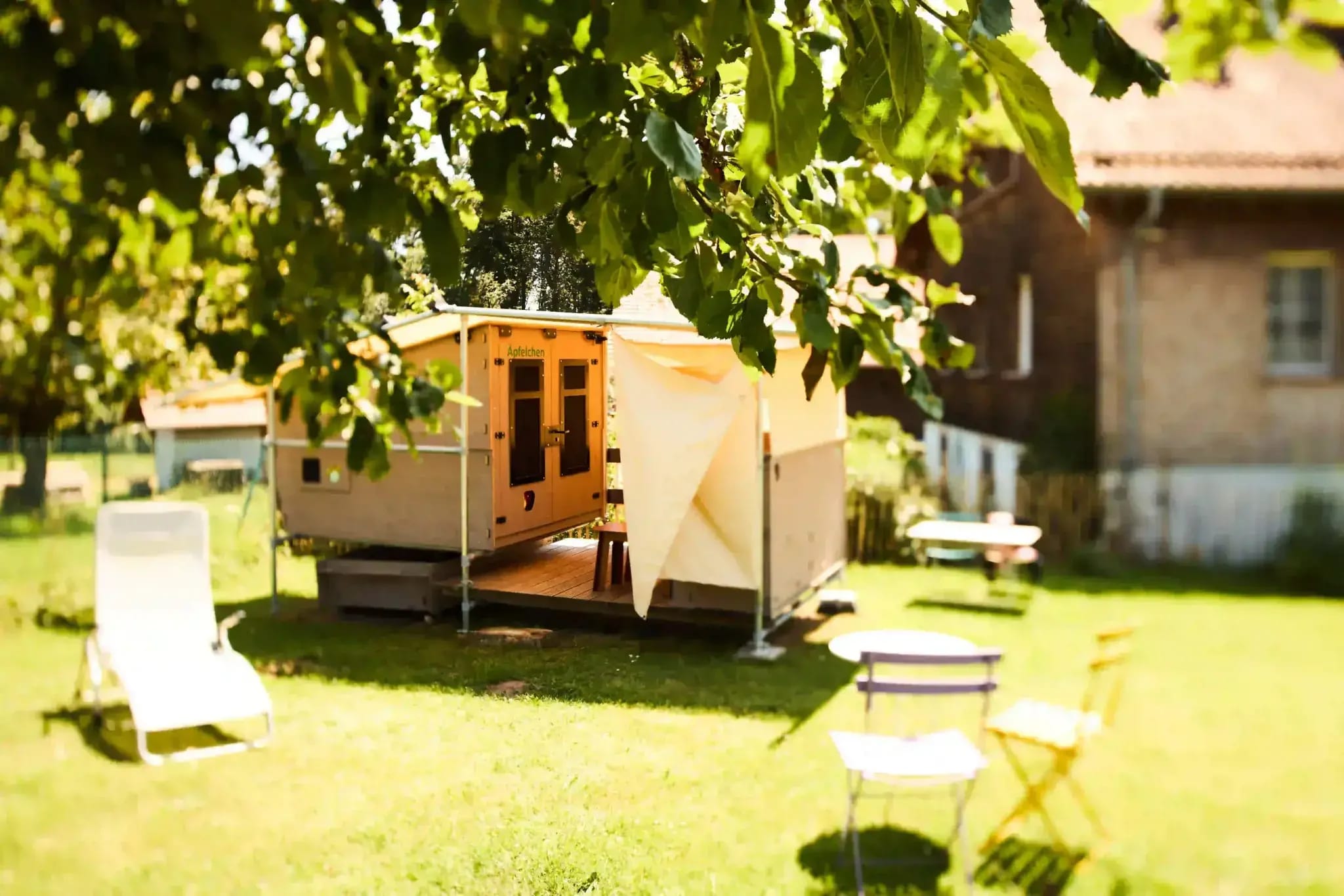 Glamping-Wagen mit Vorzelt und Liegestühlen auf der Gartenwiese