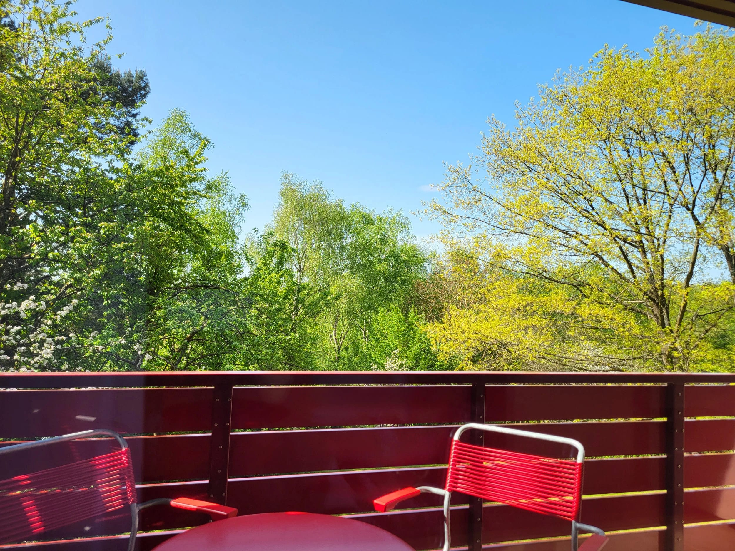 Balkon mit rotem Geländer und roten Stühlen, Blick ins Grüne
