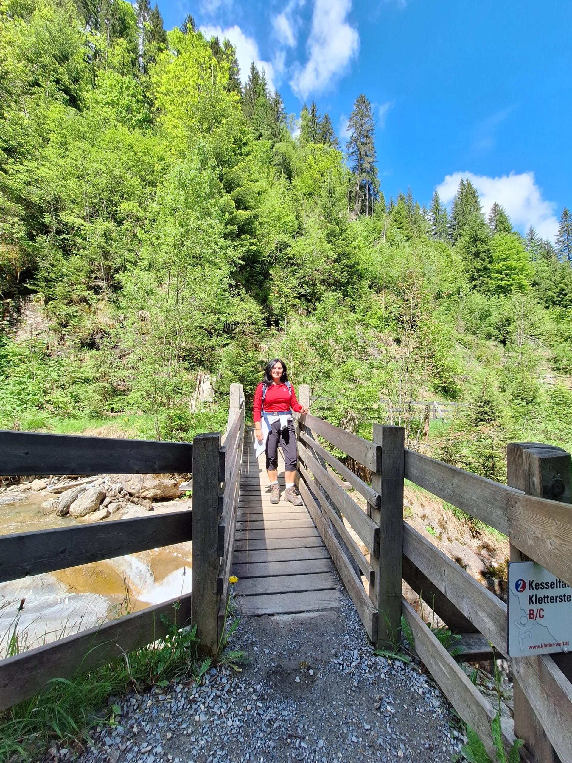 Wanderin in roter Jacke auf einer Hängebrücke im Wald