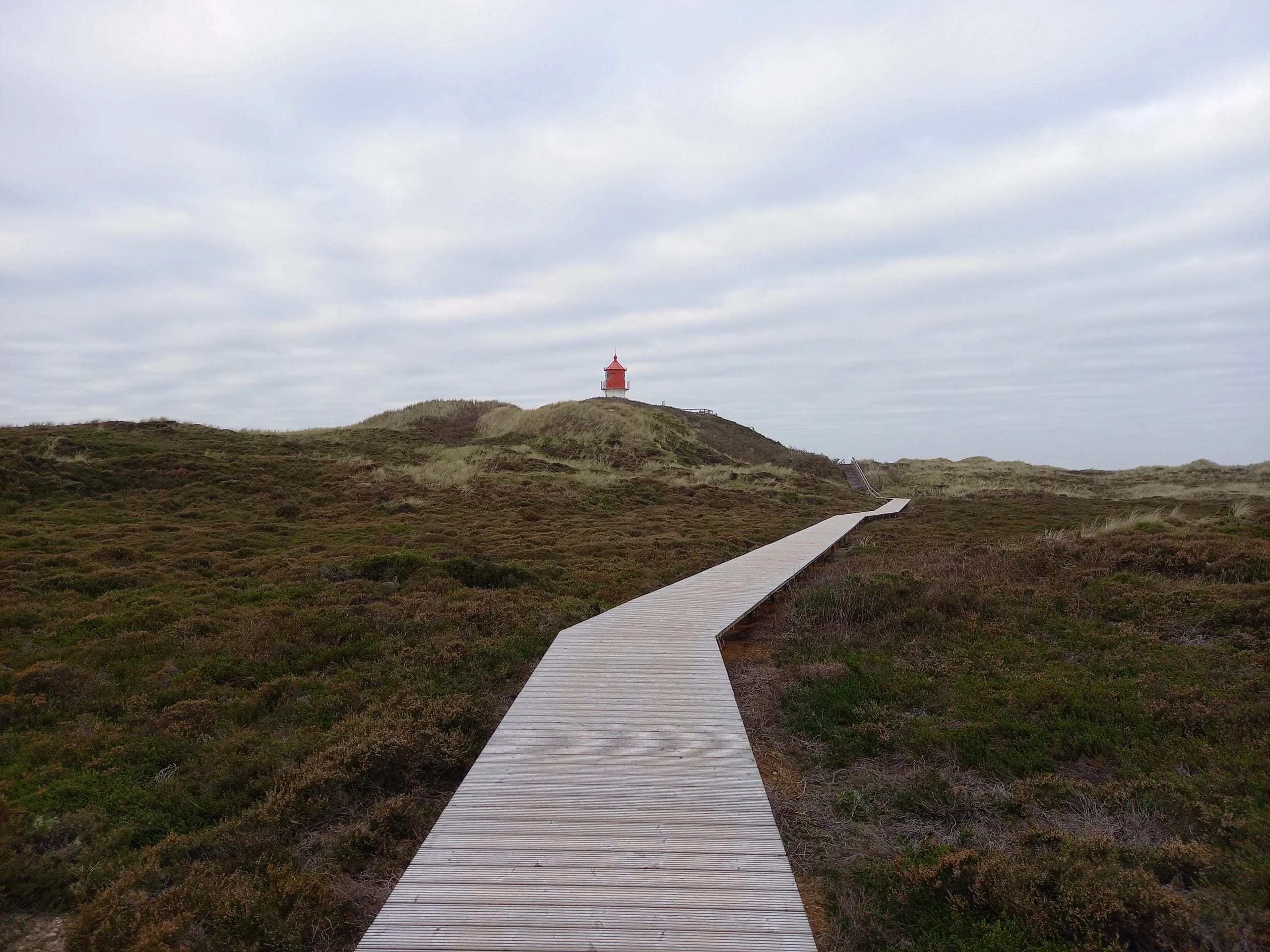 Holzsteg durch die Dünen zu einem kleinen Leuchtturm