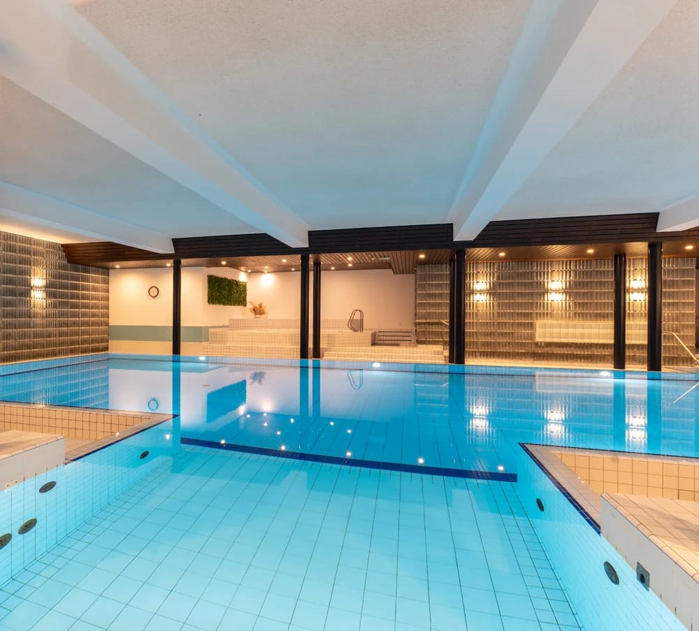 Hallenbad mit blau gefliestem Becken, Sprudelbecken und indirekter Beleuchtung