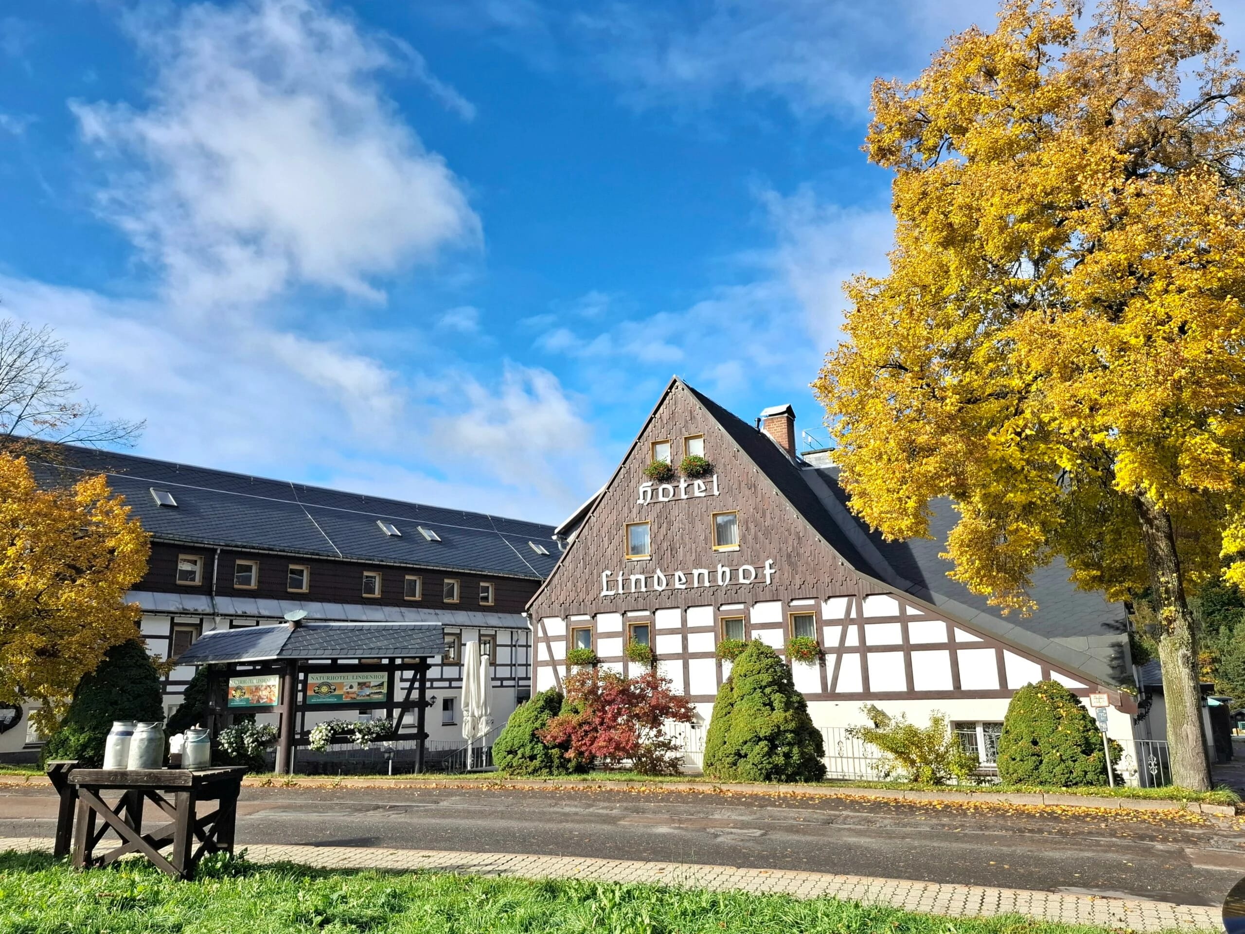 Außenansicht des Hotels mit dunkler Giebelfassade, Fachwerk und herbstlich gelb gefärbtem Baum davor
