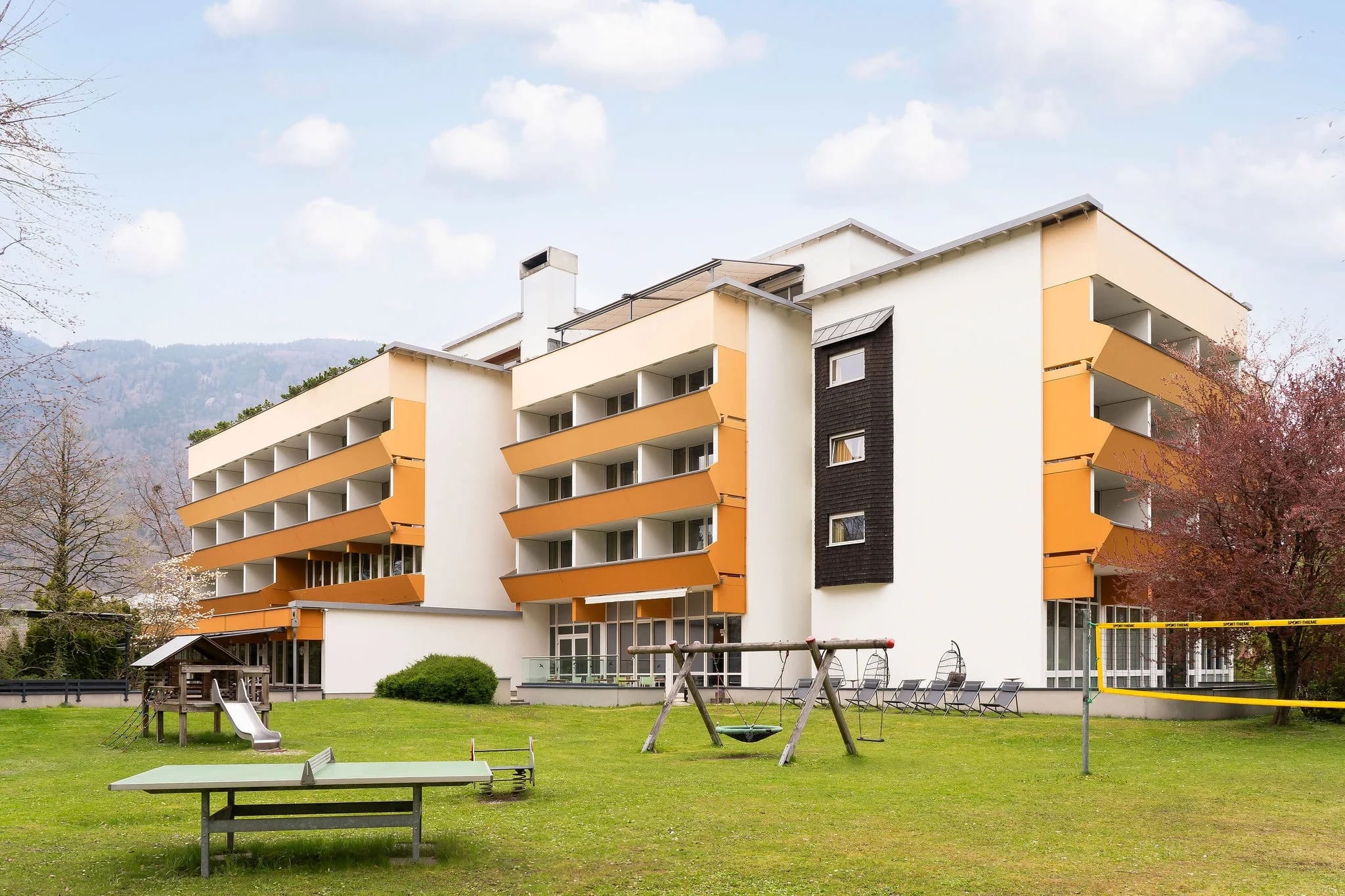 Außenansicht des Hotelgebäudes mit Liegewiese und Bergen im Hintergrund