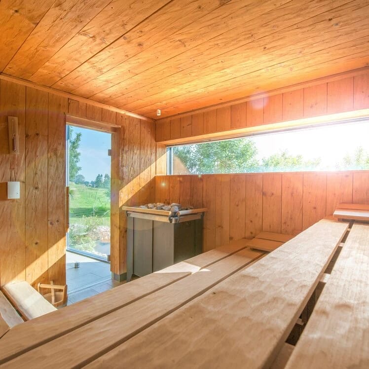 Sauna mit breiten Holzbänken, Saunaofen und Fenster ins Grüne