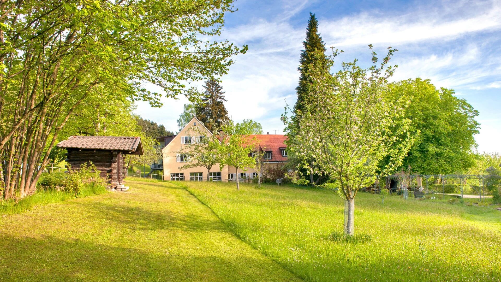 Gartenseite des Hauses mit weitläufiger Wiese, Obstbäumen und Holzhütte
