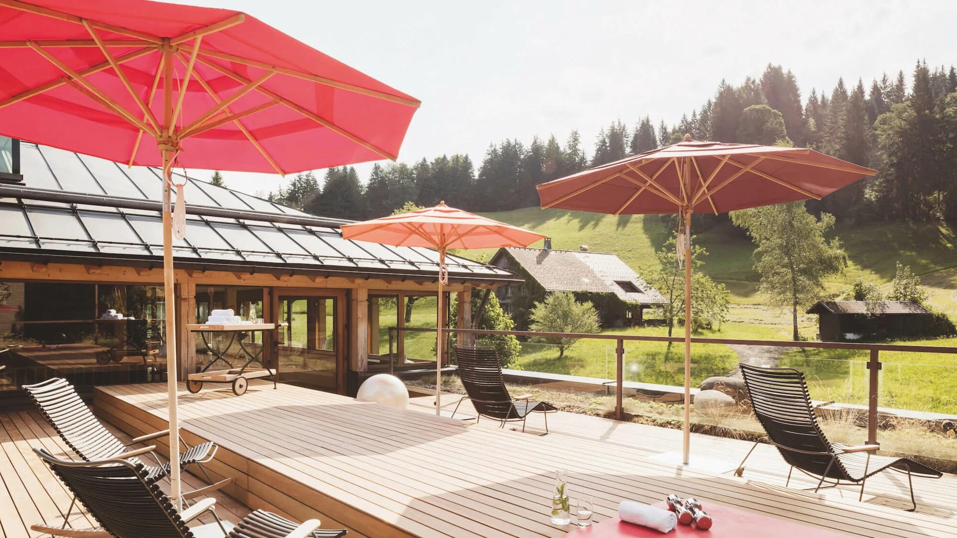Sonnenterrasse mit Holzdeck, roten Sonnenschirmen und Liegestühlen