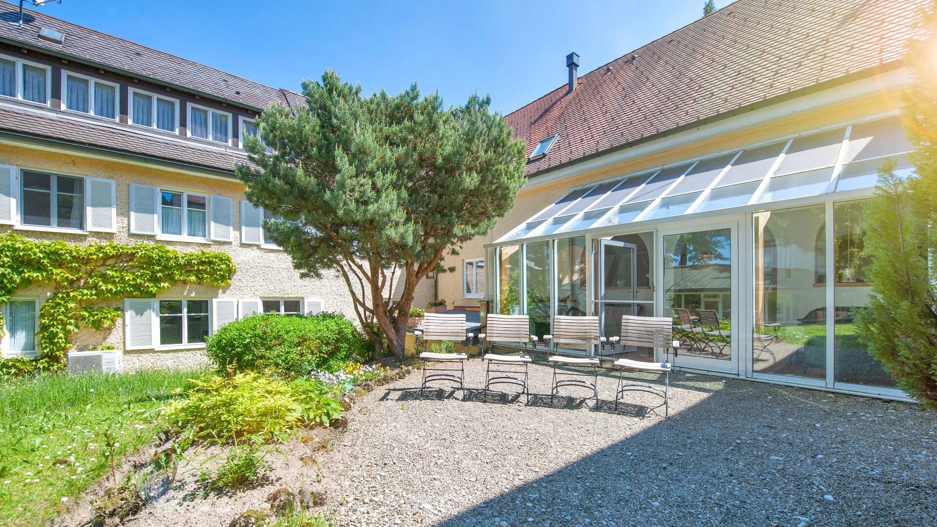 Innenhof mit Kiesterrasse, Loungesesseln und großer Kiefer vor dem Wintergarten