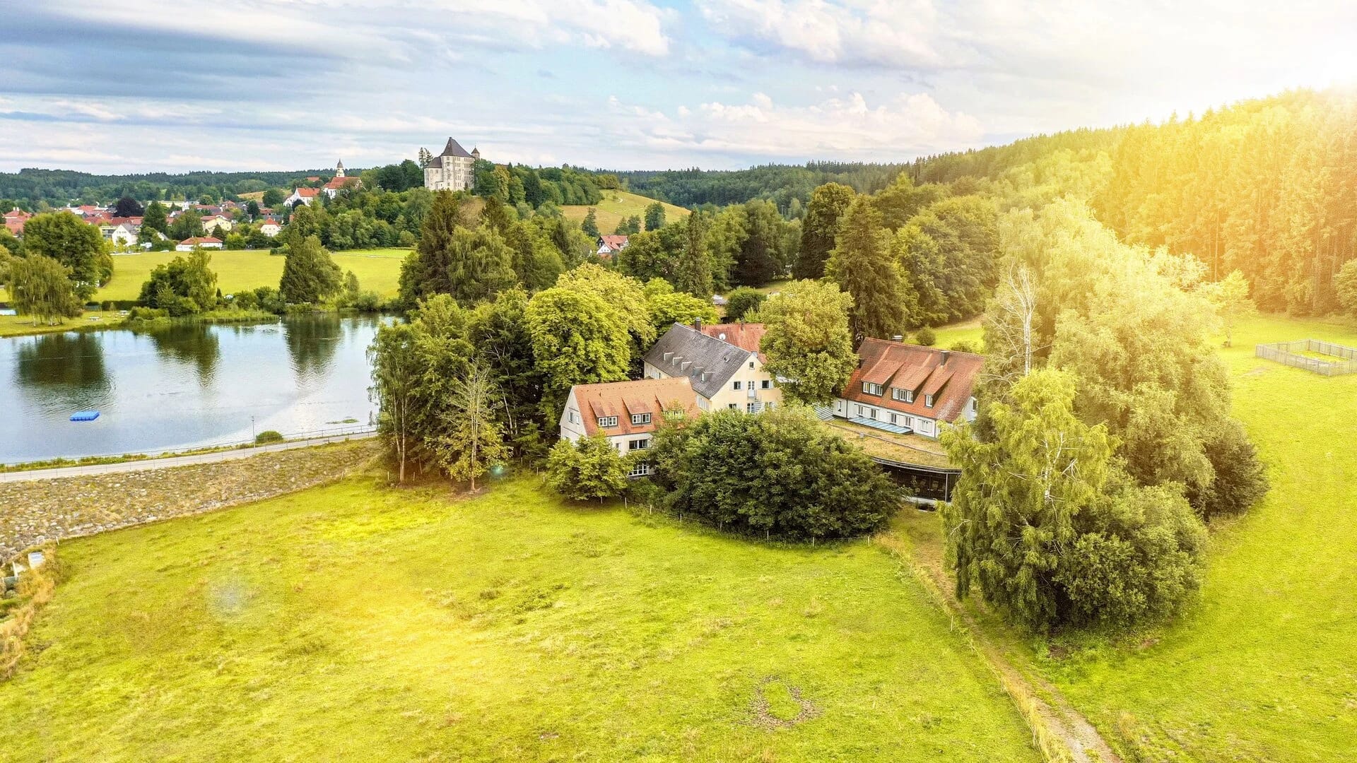Luftbild des Hauses direkt am See, umgeben von Wiesen und Wald
