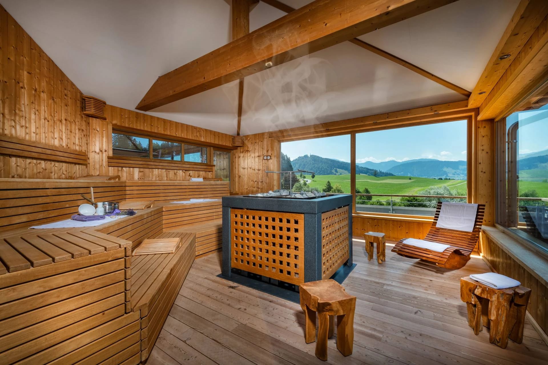Panoramasauna aus Holz mit Saunaofen, Liegen und großen Fenstern zur Berglandschaft