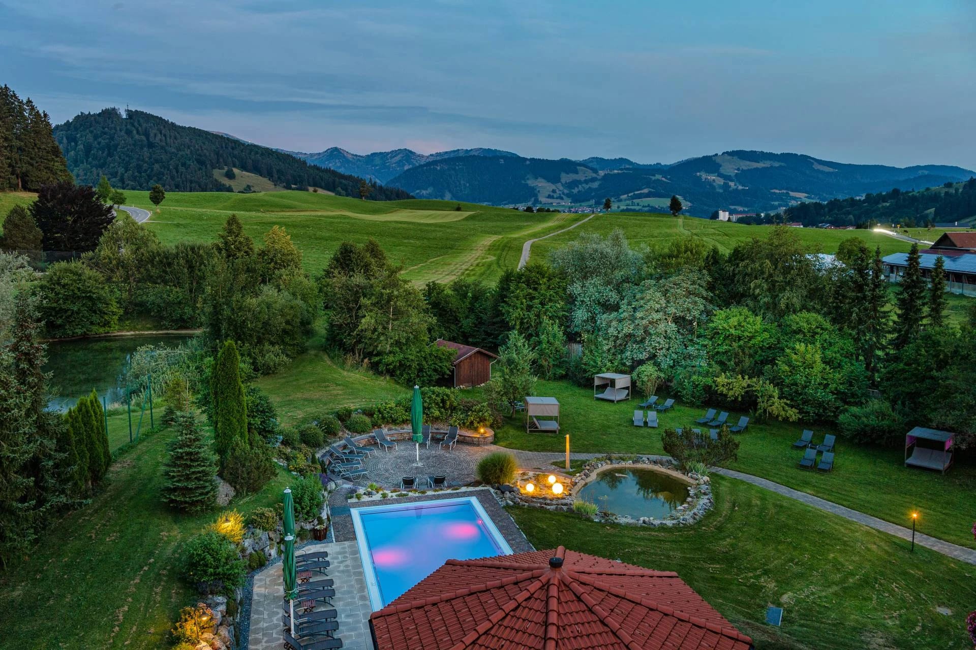 Abendlicher Blick über die Gartenanlage mit beleuchtetem Außenpool und Bergpanorama