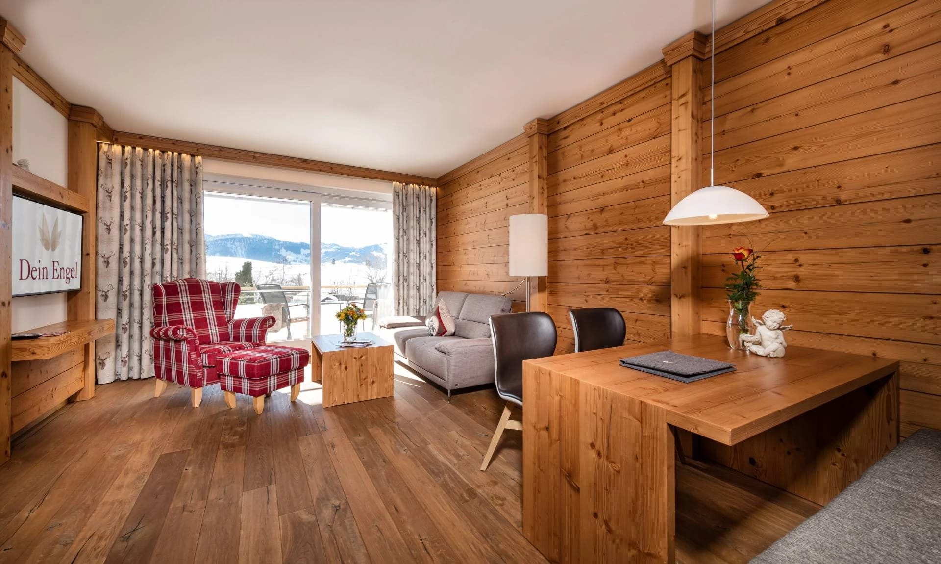 Wohnbereich einer Suite mit Holzvertäfelung, kariertem Ohrensessel und Schreibtisch am Panoramafenster