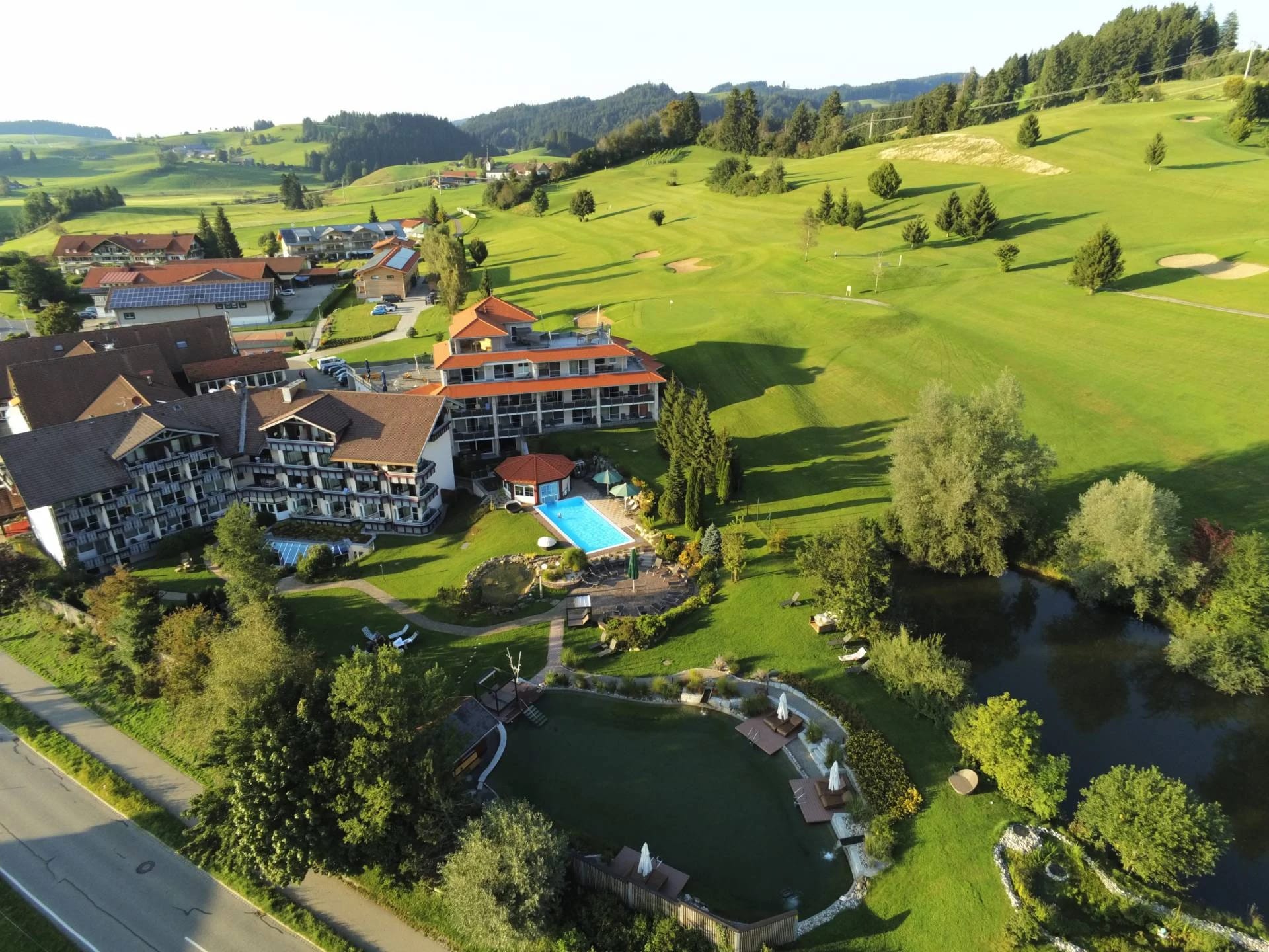 Luftaufnahme der Hotelanlage mit Garten, Außenpool, Naturteich und angrenzendem Golfplatz