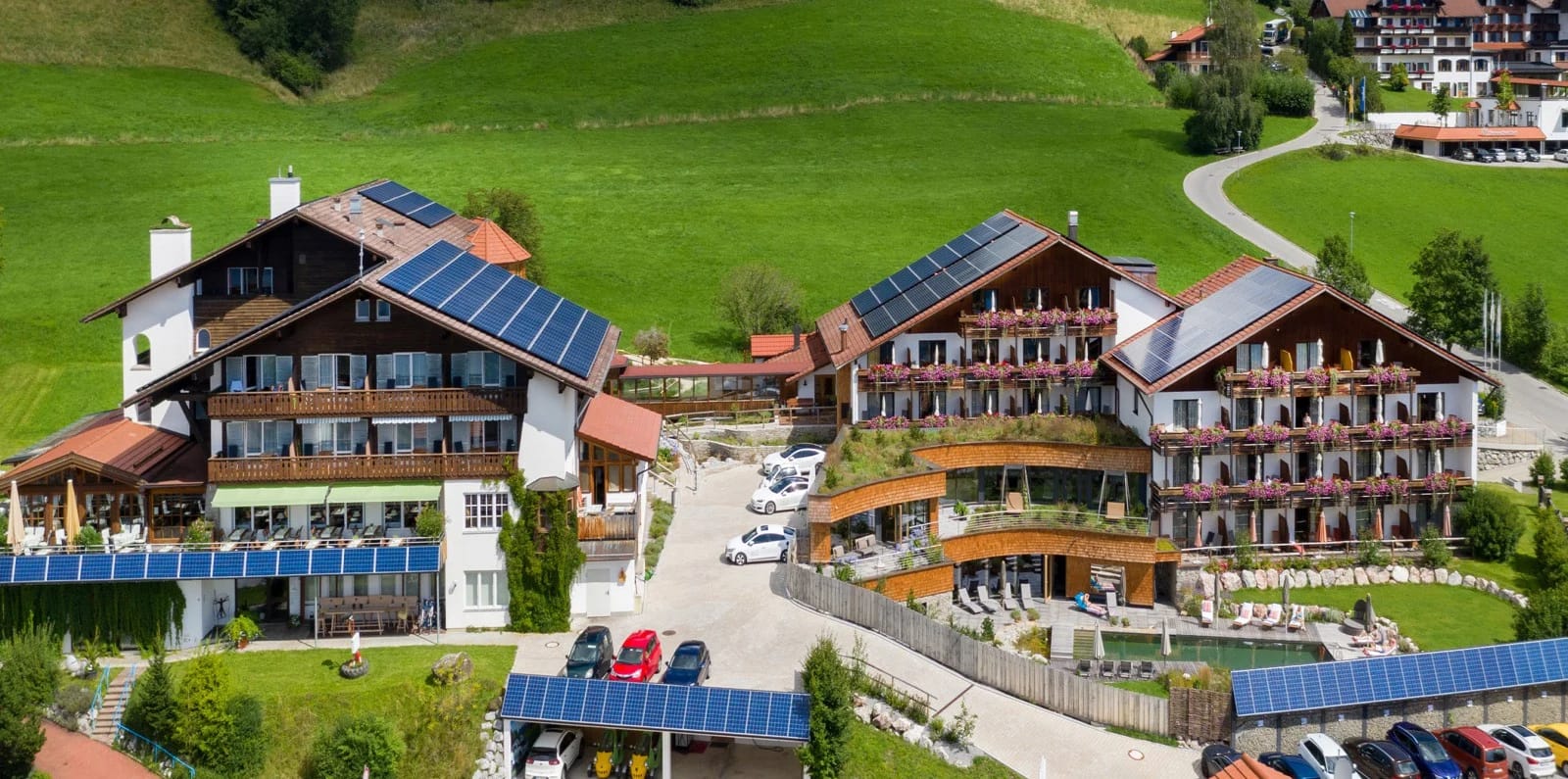 Außenansicht der beiden Hotelgebäude mit Balkonen und Solardächern vor grünen Wiesen