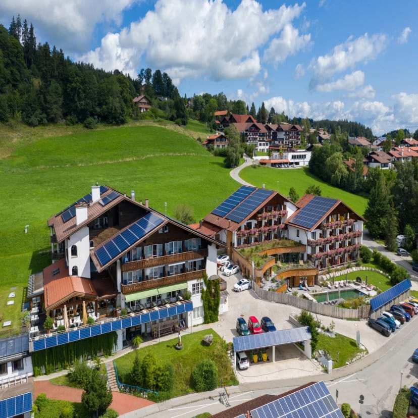 Luftaufnahme des Biohotels Eggensberger mit Solardächern, eingebettet in die grüne Allgäuer Hügellandschaft