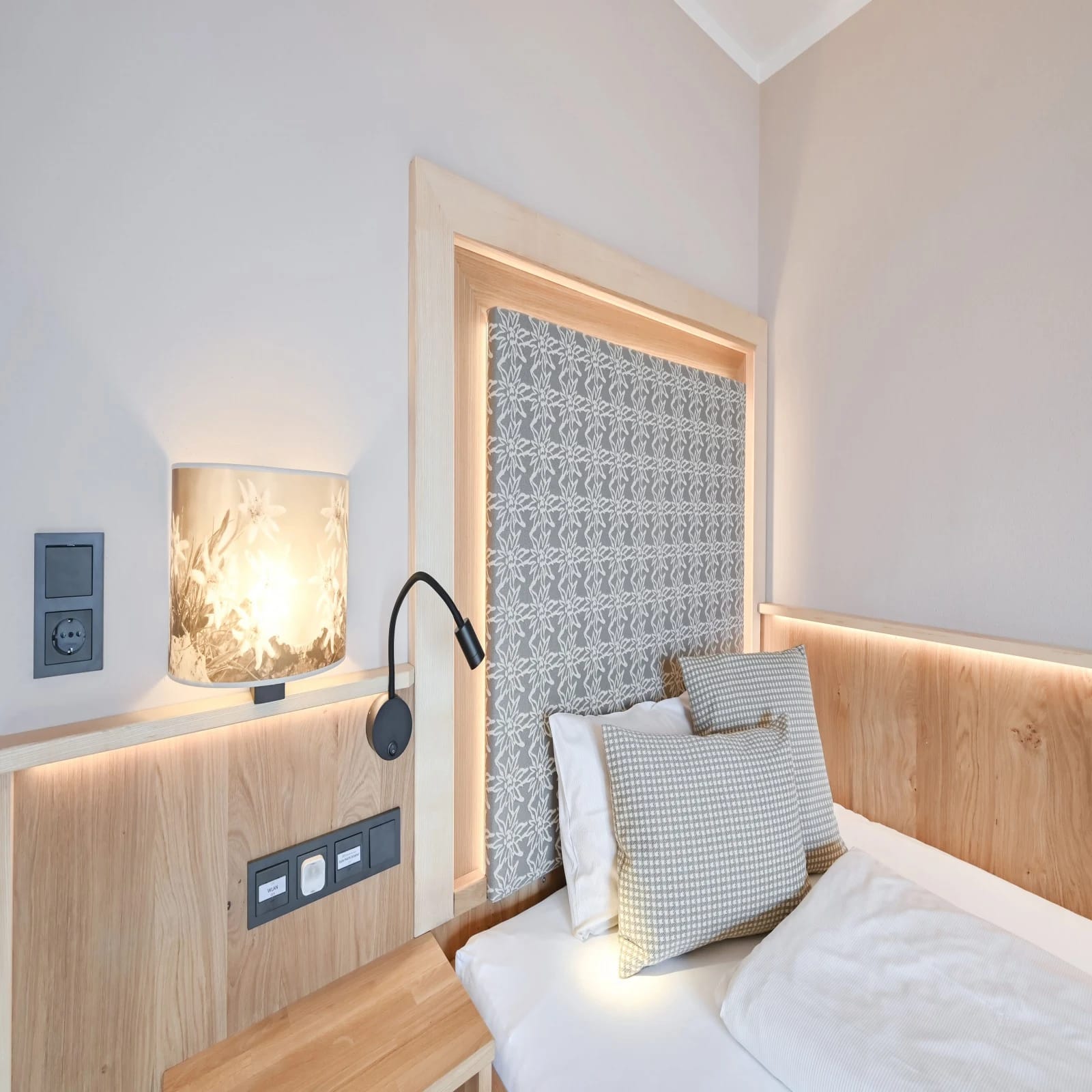Helles Zimmer mit Doppelbett, hellem Holz und gemustertem Kopfteil
