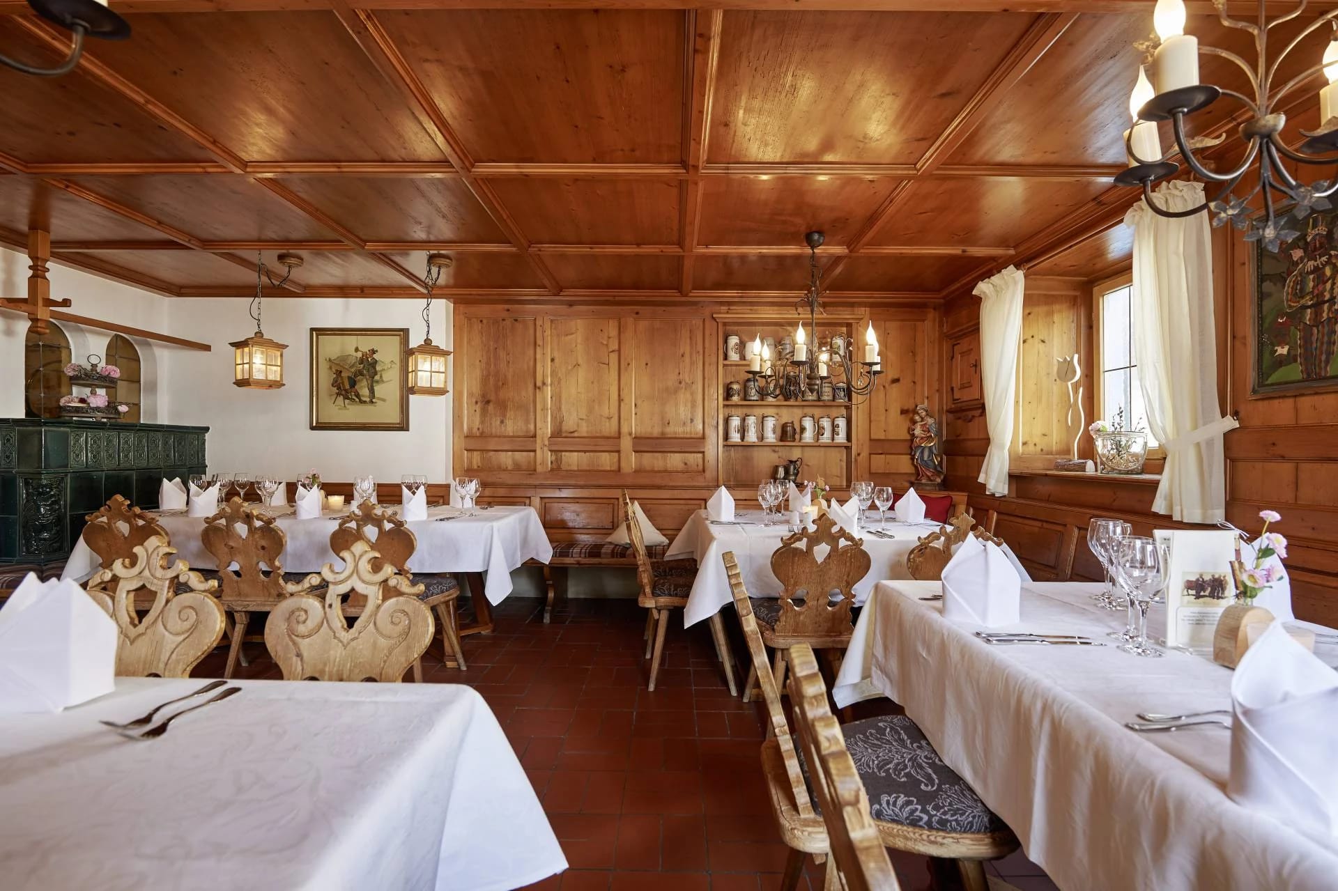 Holzgetäfelte Stube mit weiß eingedeckten Tischen, geschnitzten Stühlen und Kronleuchter