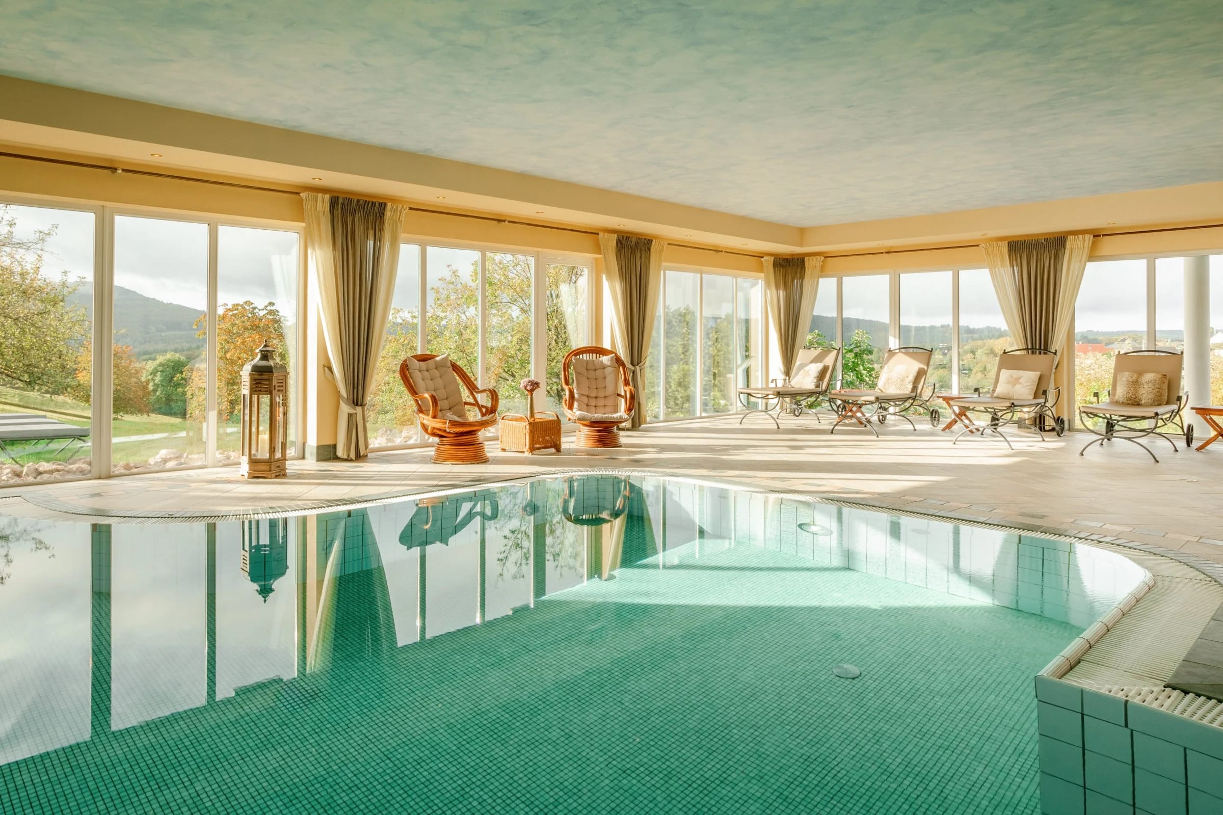 Hallenbad mit grün schimmerndem Wasser und Panoramafenstern zur Landschaft
