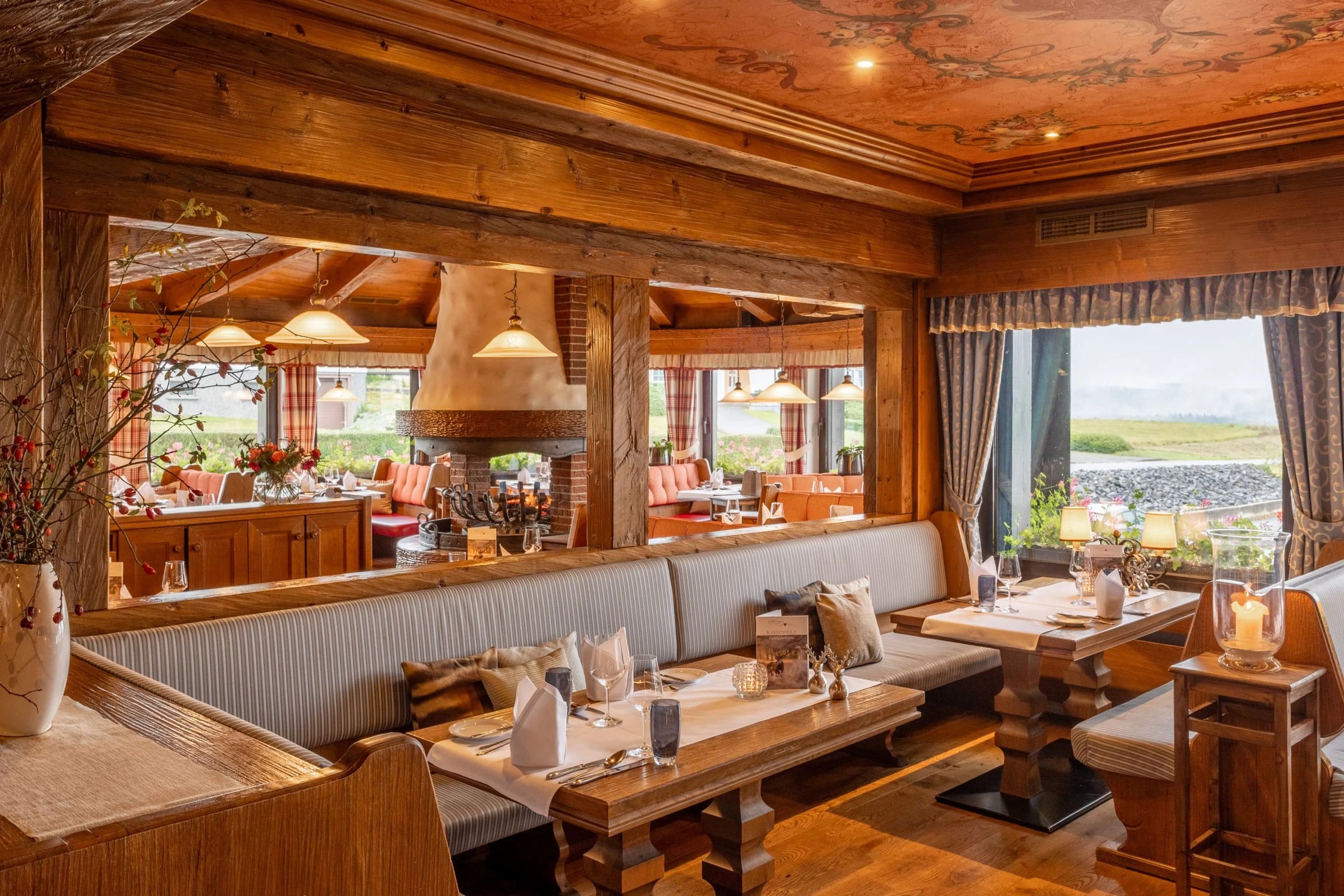 Restaurantstube mit Holzvertäfelung, offenem Kamin und Fensterfront ins Grüne