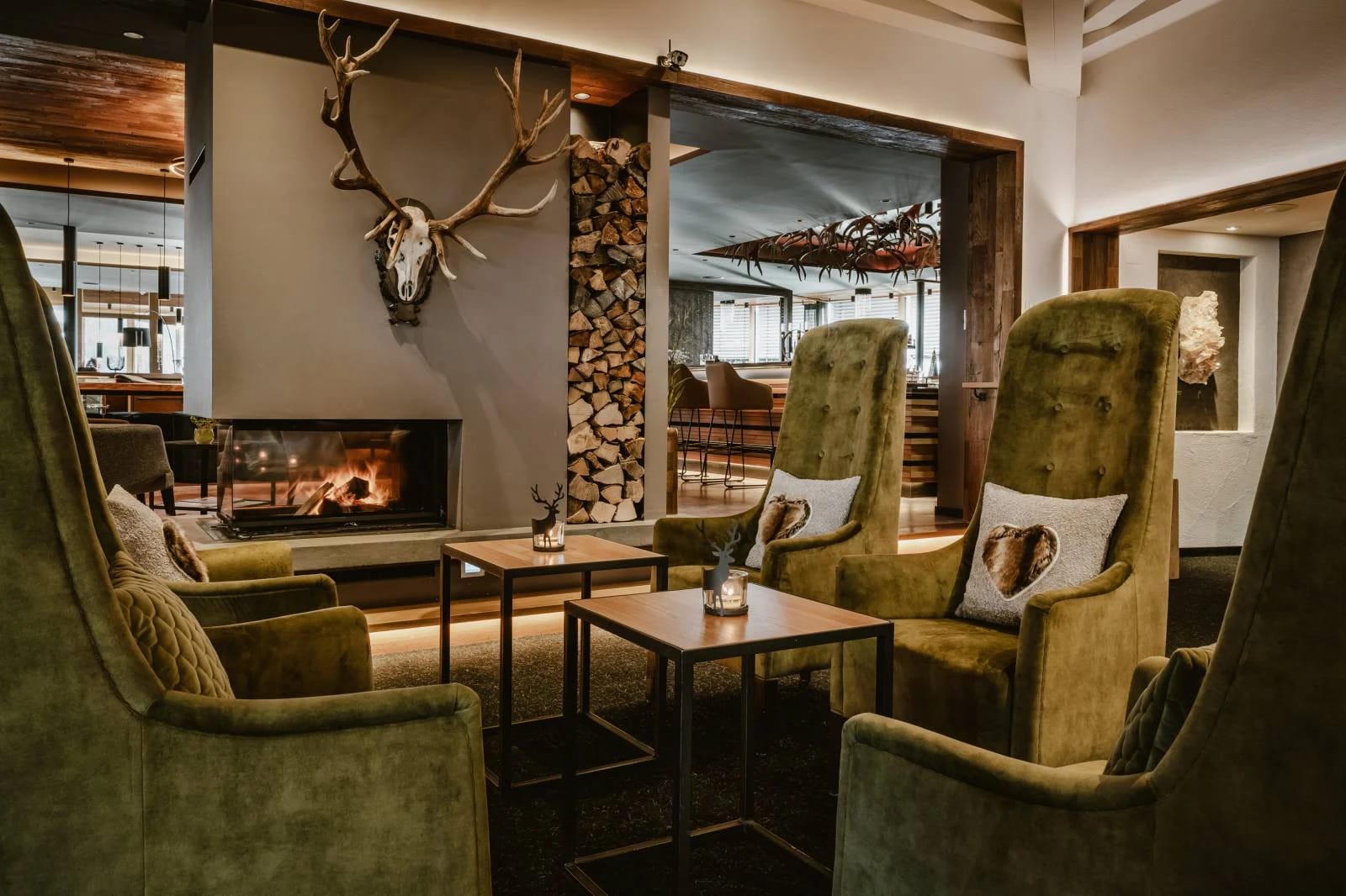 Lounge mit offenem Kamin, hohen Polstersesseln und Geweih an der Wand