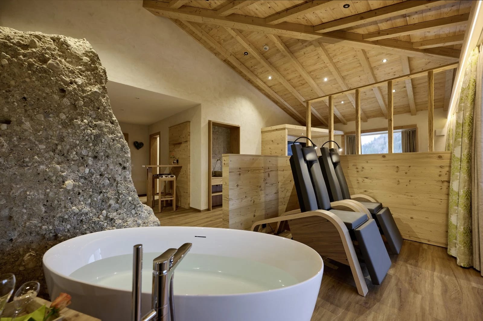 Zimmer mit freistehender runder Badewanne, Natursteinwand und zwei Relaxliegen