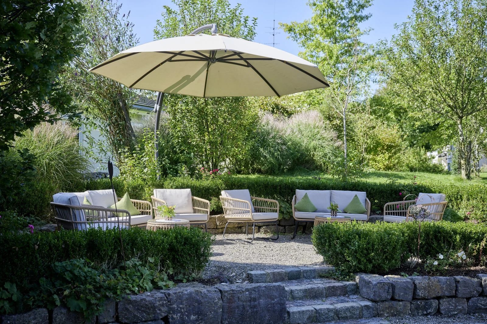 Gartenlounge mit Polstermöbeln unter großem Sonnenschirm, Hecken und Natursteintreppe
