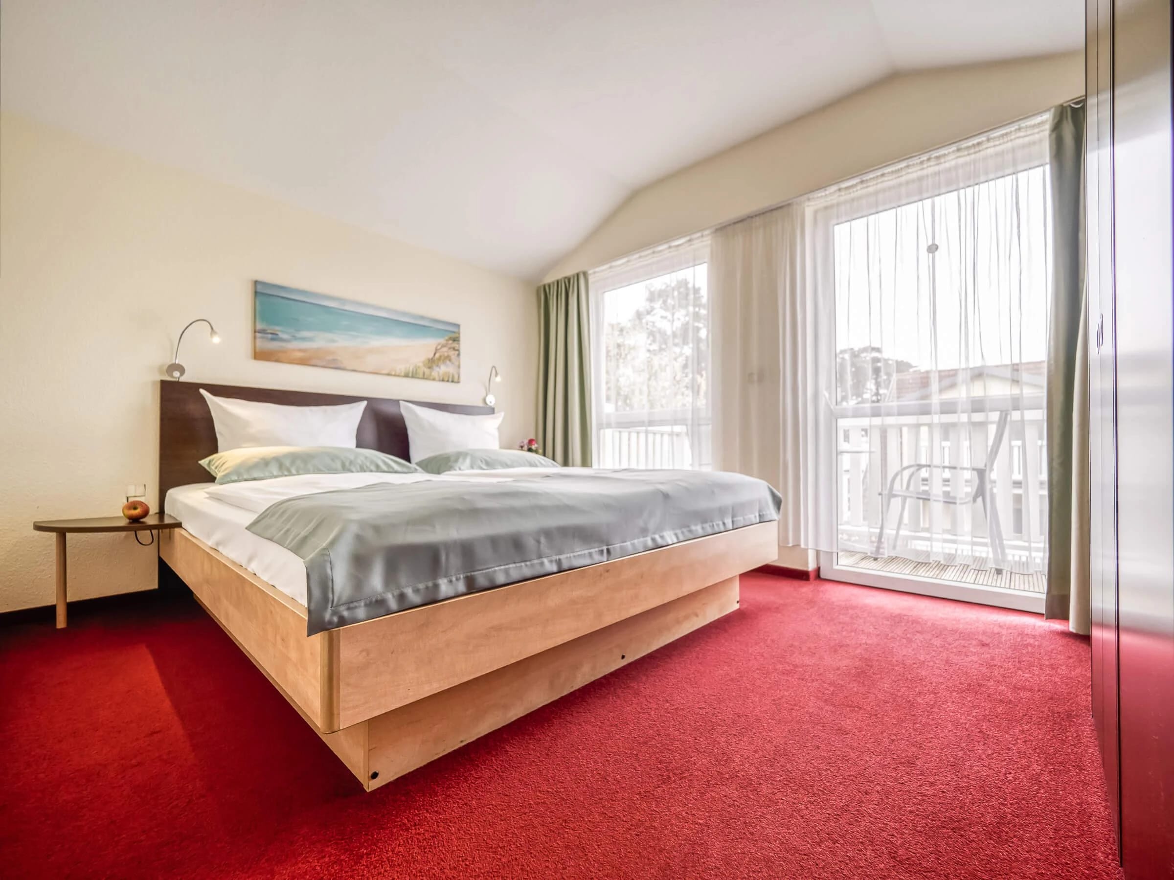 Zimmer mit Doppelbett, rotem Teppich und Balkontür