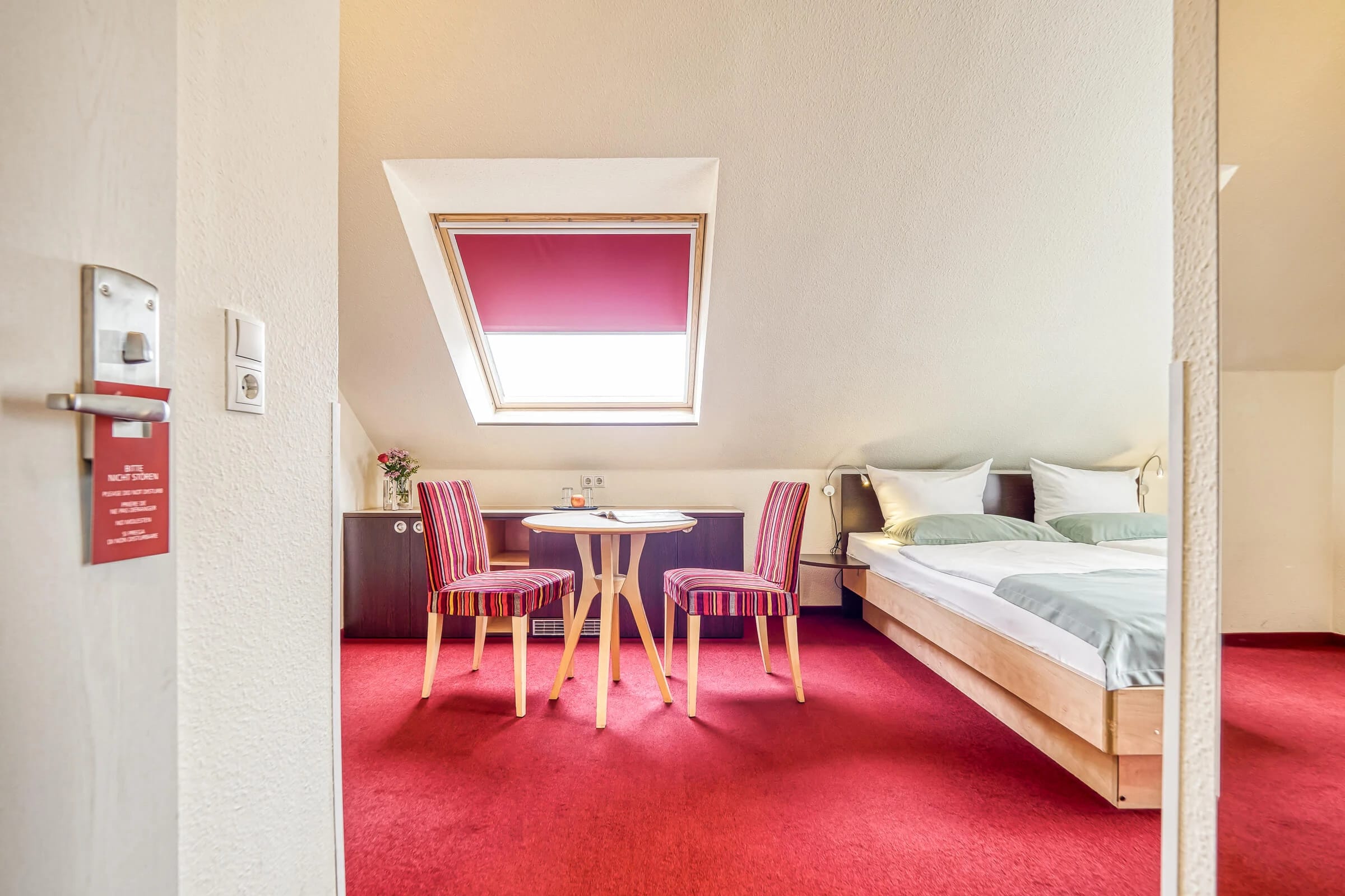 Dachgeschosszimmer mit Dachfenster, Bett und kleiner Sitzgruppe