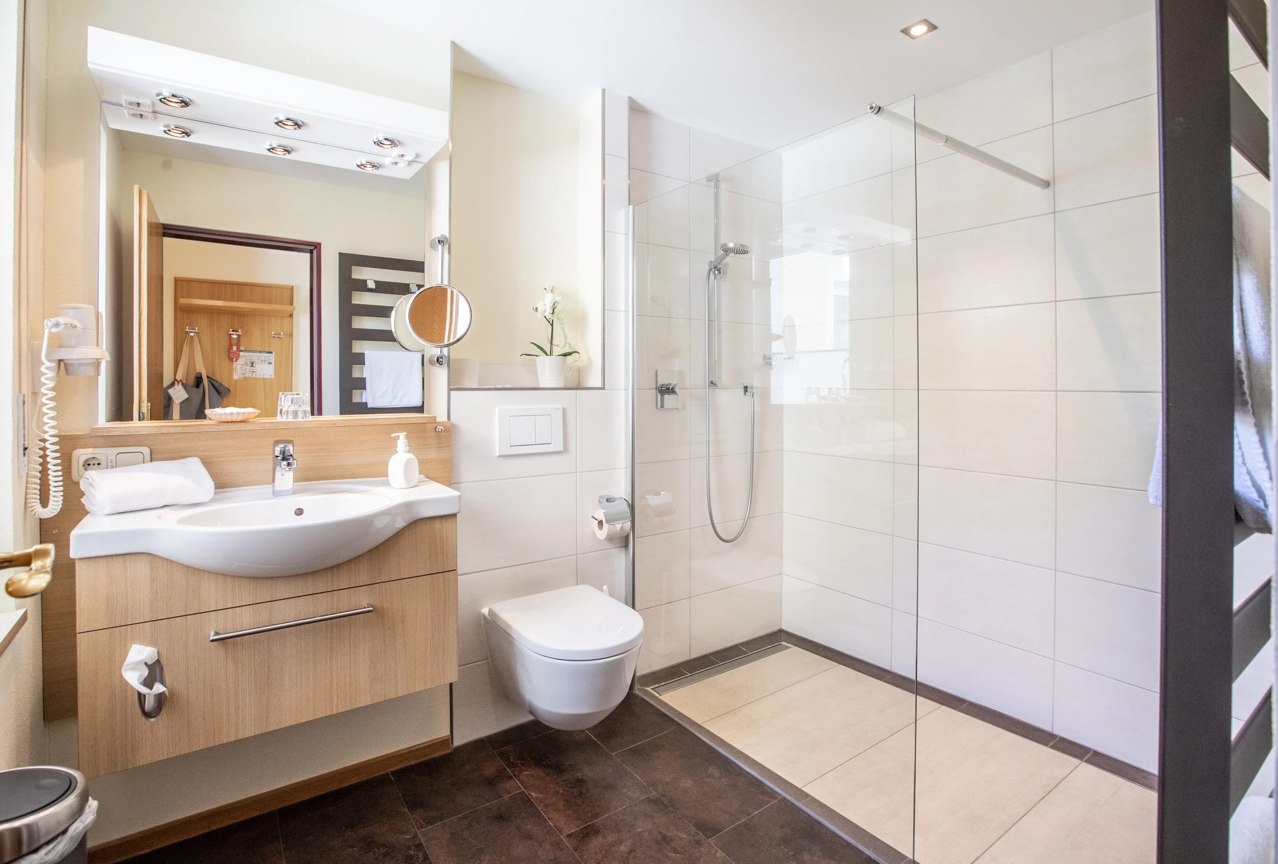 Badezimmer mit ebenerdiger Glasdusche, Waschtisch und beleuchtetem Spiegel