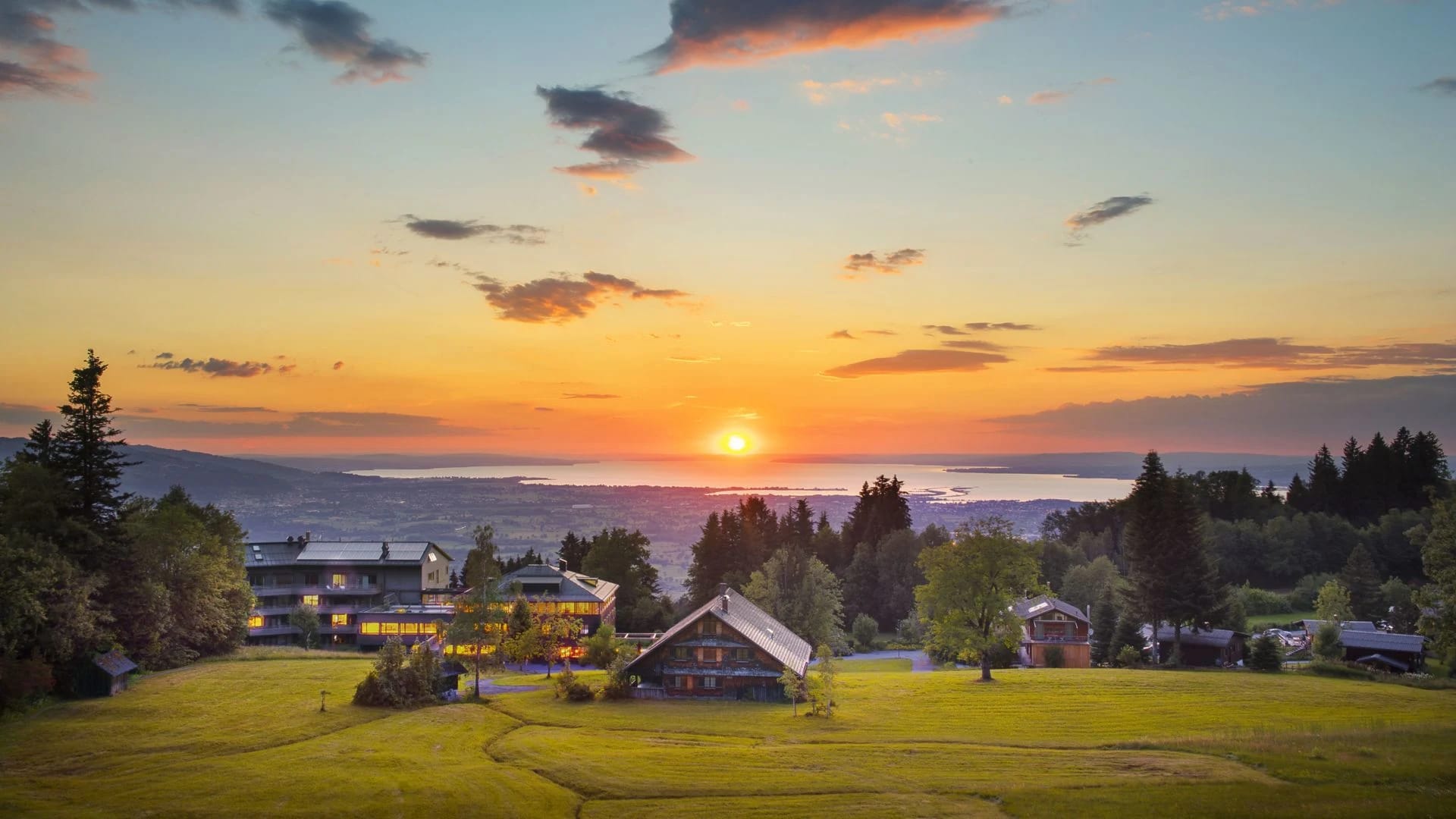 Gebäude des Hauses in Wiesen bei Sonnenuntergang, Blick über das Tal zum See